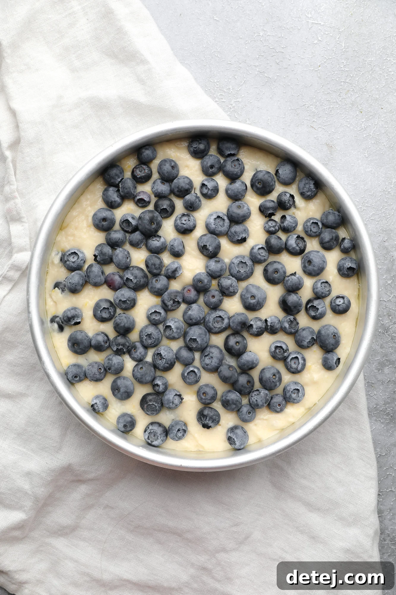blueberry cake batter with fresh blueberries on top in a round metal cake pan.