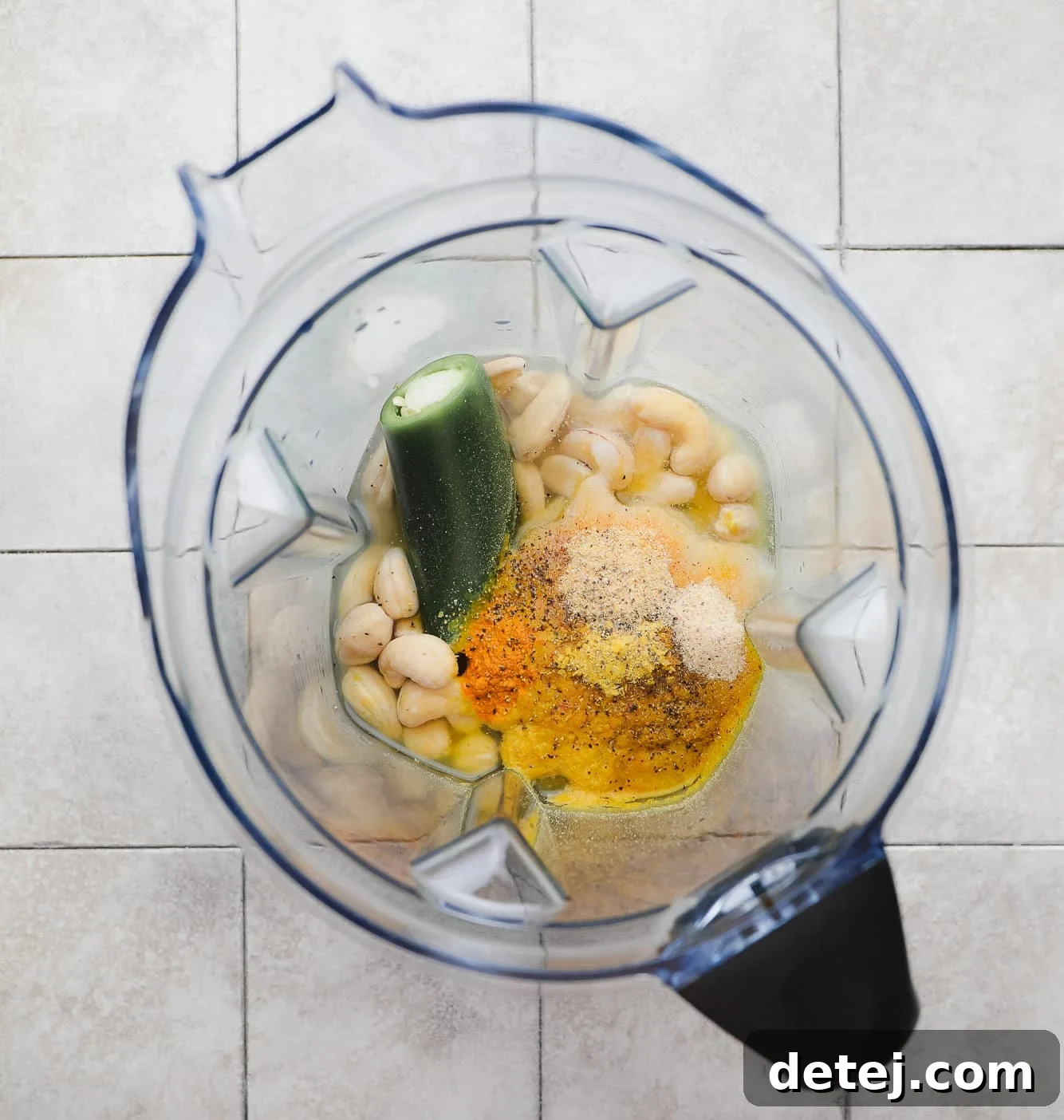 All the ingredients for the creamy cashew cheese sauce, including cashews, jalapeño, and spices, are assembled in a large blender, ready for blending.