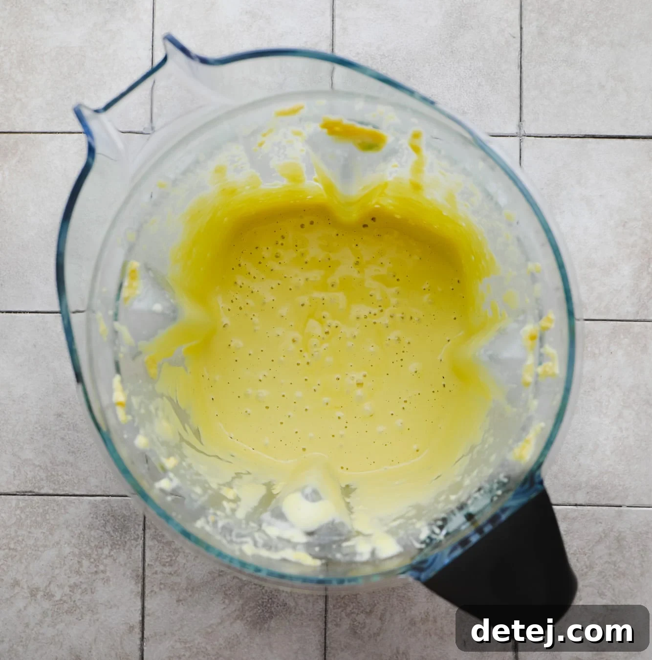 Smooth, blended yellow cashew cheese sauce swirls dynamically in a large blender, showcasing its creamy and rich texture after processing.