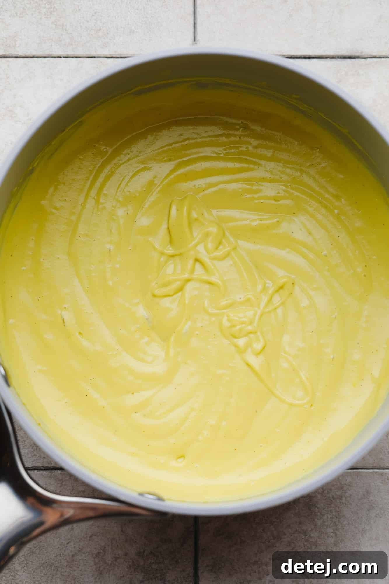 Vibrant yellow cashew cheese sauce simmering gently in a sleek grey saucepan on the stovetop, ready to be served.