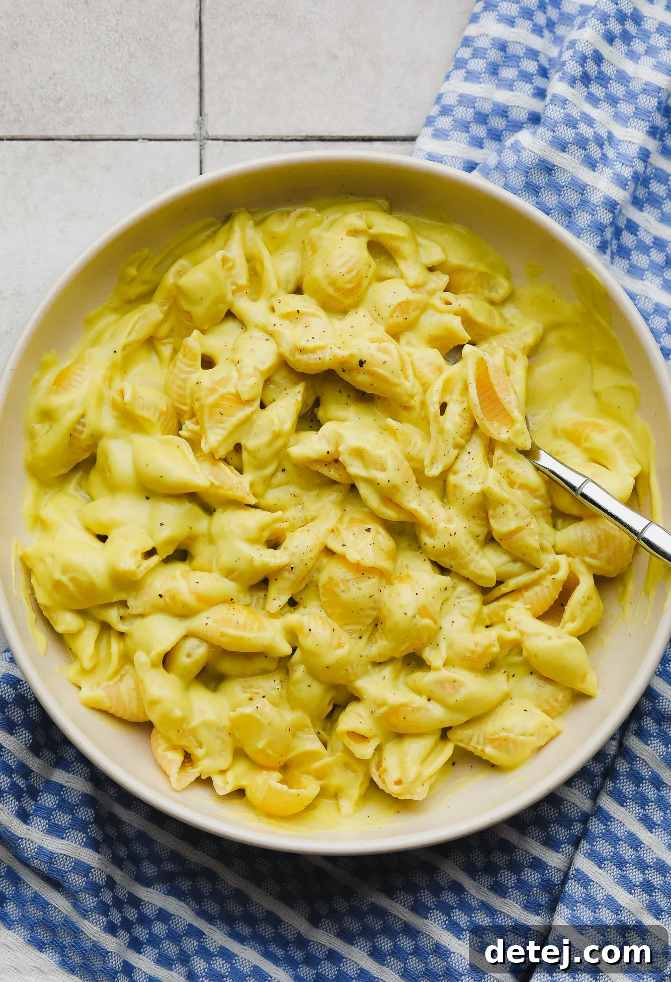 A beige bowl filled with creamy vegan mac and cheese, featuring bright yellow pasta coated in a rich, smooth sauce.