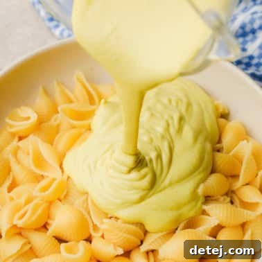 pouring yellow cashew cheese sauce over a large bowl of cooked pasta.
