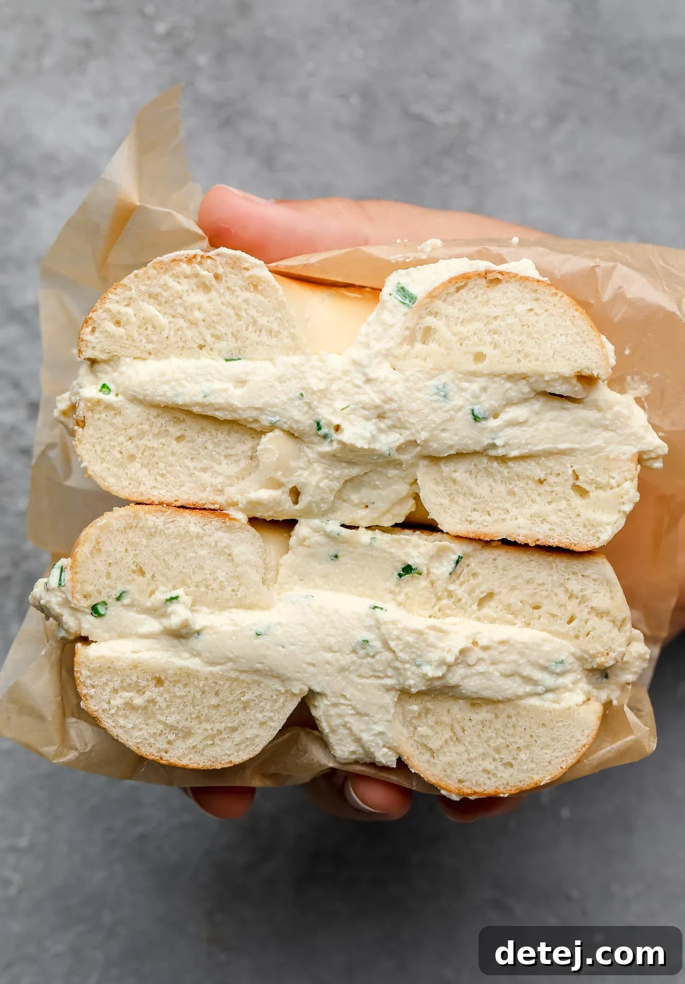 A woman's hand holding a vegan cream cheese bagel cut in half, showcasing the creamy texture.