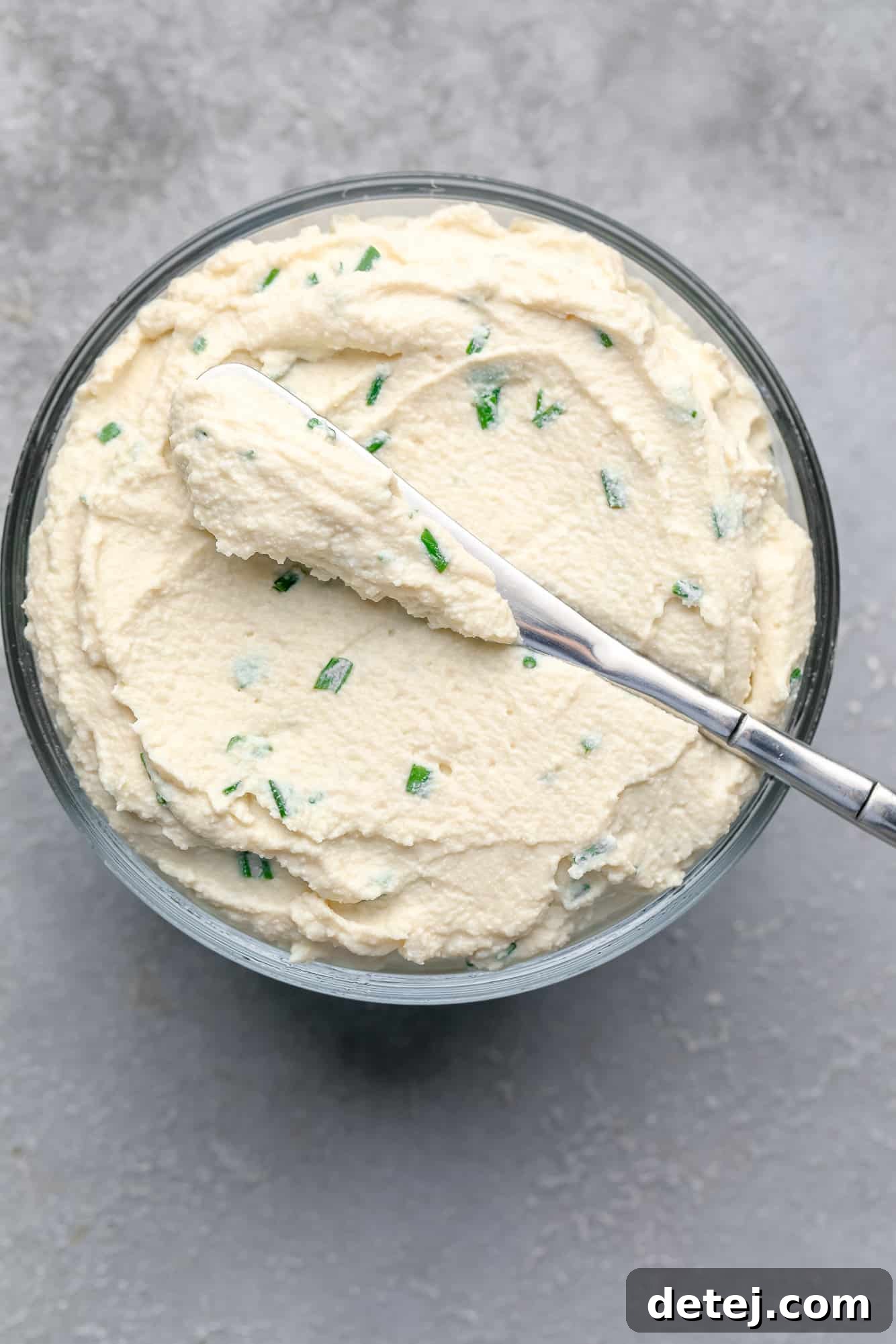 Tofu cream cheese presented in an elegant glass container with a spreading knife.