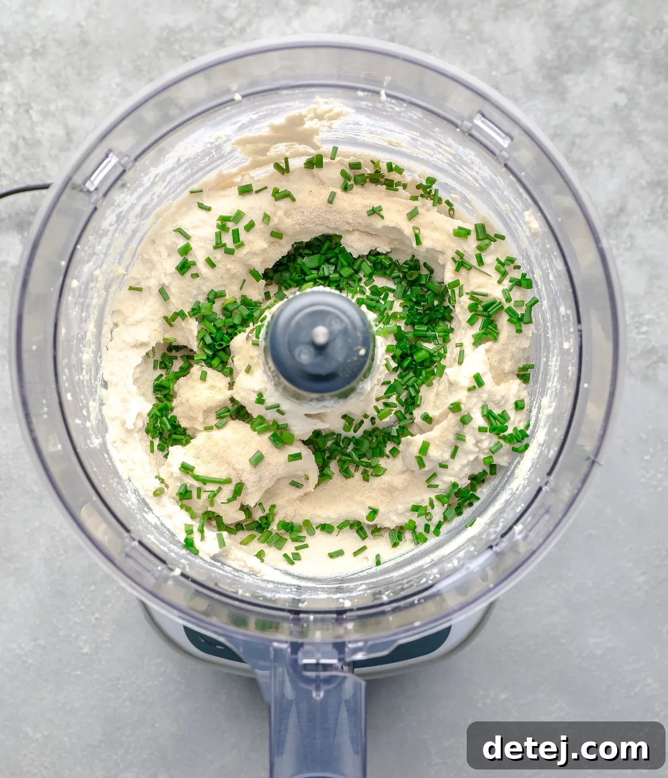 Freshly chopped chives generously sprinkled over blended tofu cream cheese in a food processor, ready for the final mix.