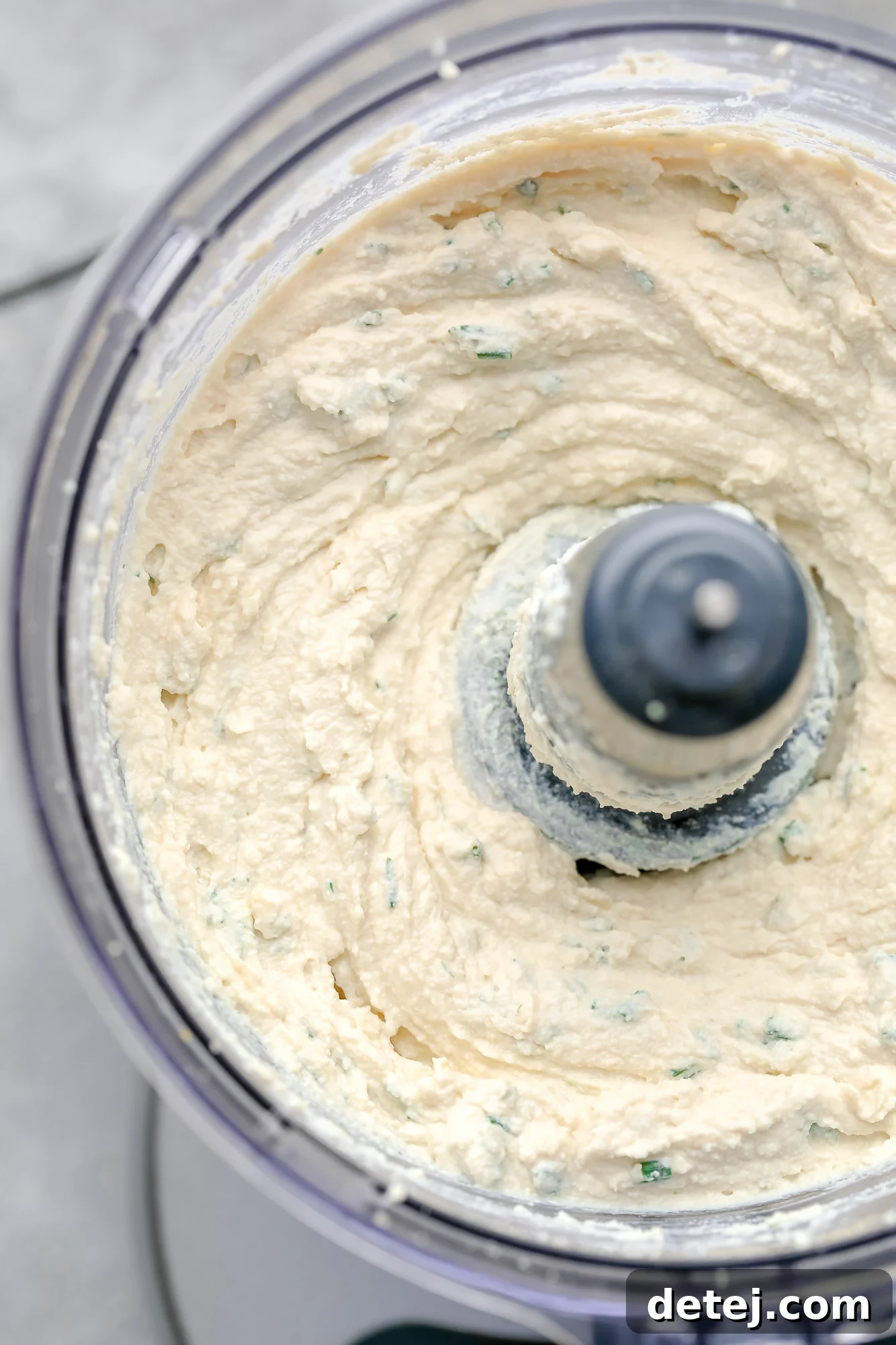 Close-up view of perfectly blended tofu cream cheese within a food processor bowl, showing its smooth and creamy texture.