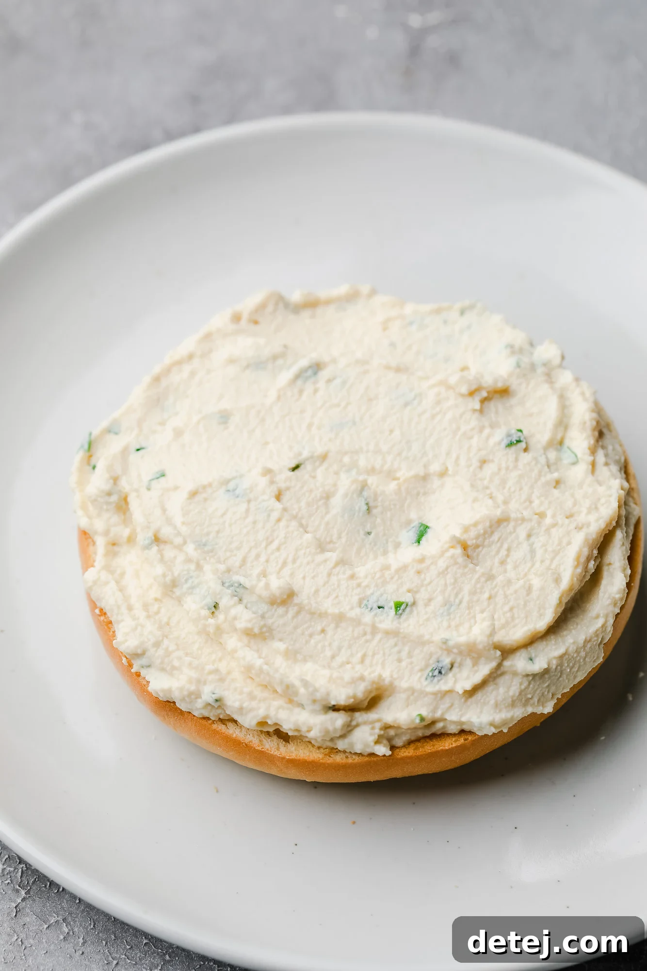 A perfectly toasted bagel on a pristine white plate, generously topped with creamy homemade tofu cream cheese, ready to be enjoyed.