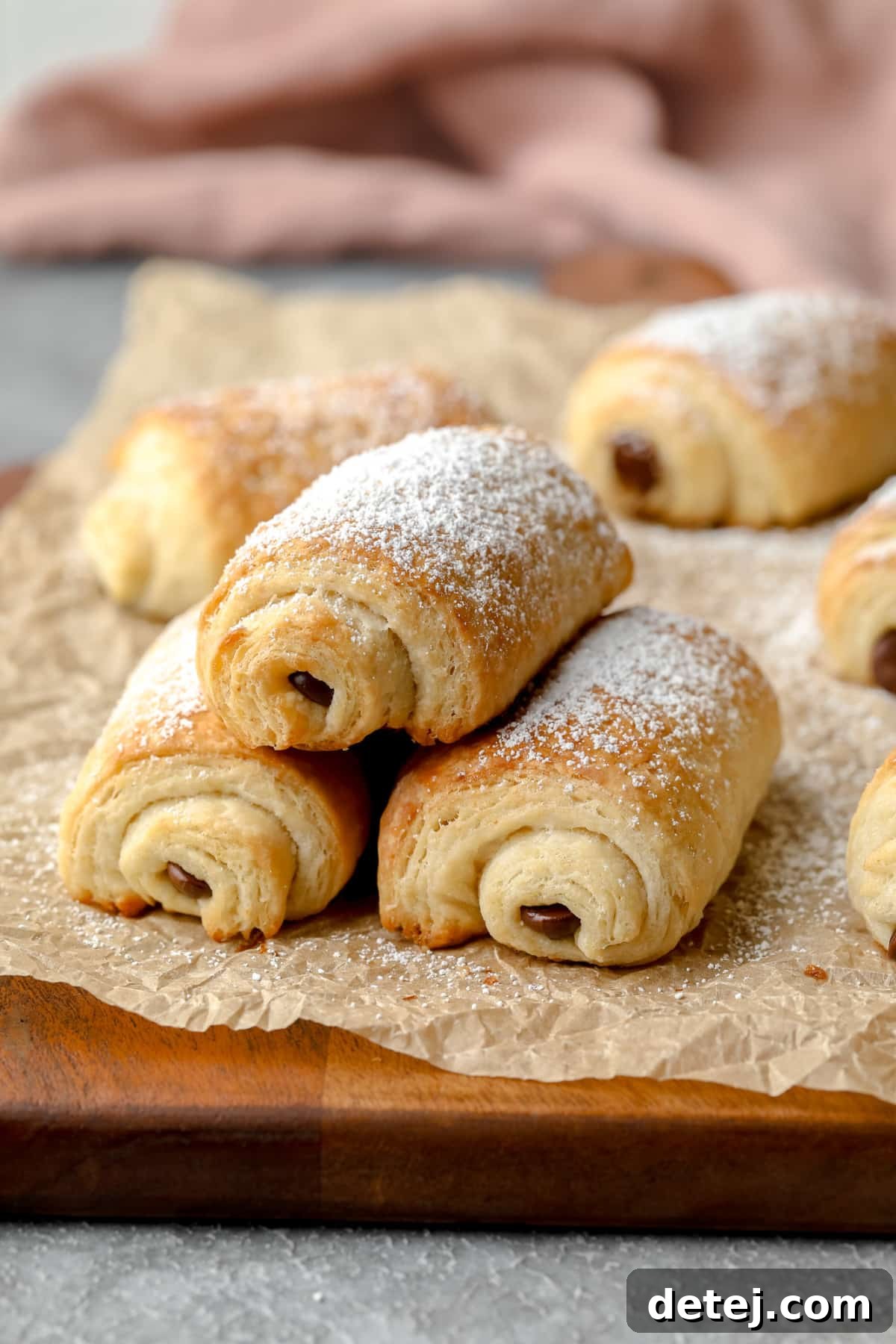 Vegan Chocolate Croissant Perfection 7 3 vegan pain au chocolat stacked on crinkly parchment paper with pink towel in background and more croissants