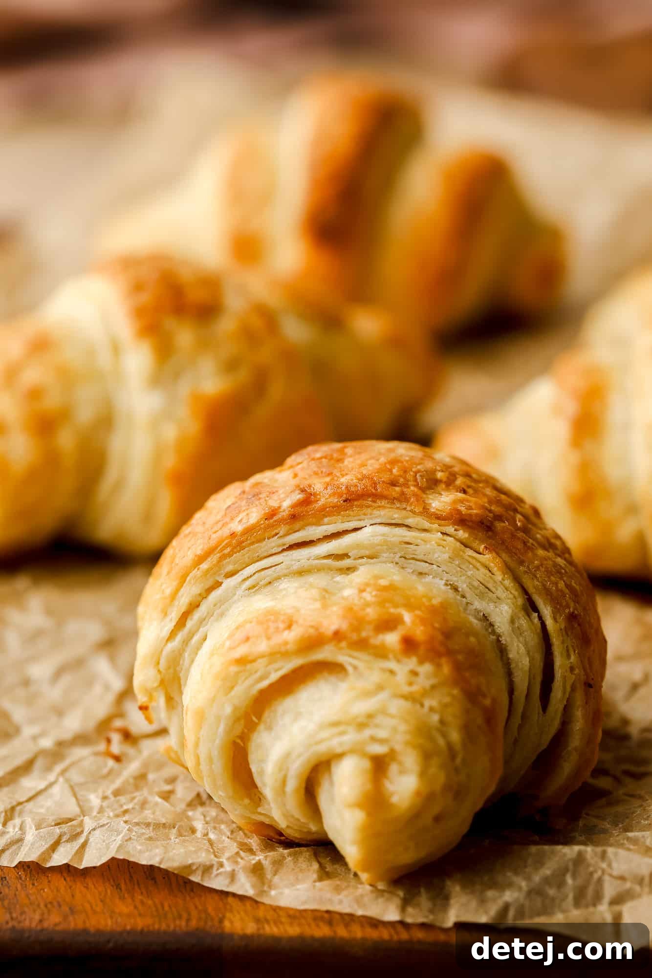 Close up on a perfectly golden-brown vegan croissant on a sheet of parchment paper, highlighting its flaky layers.