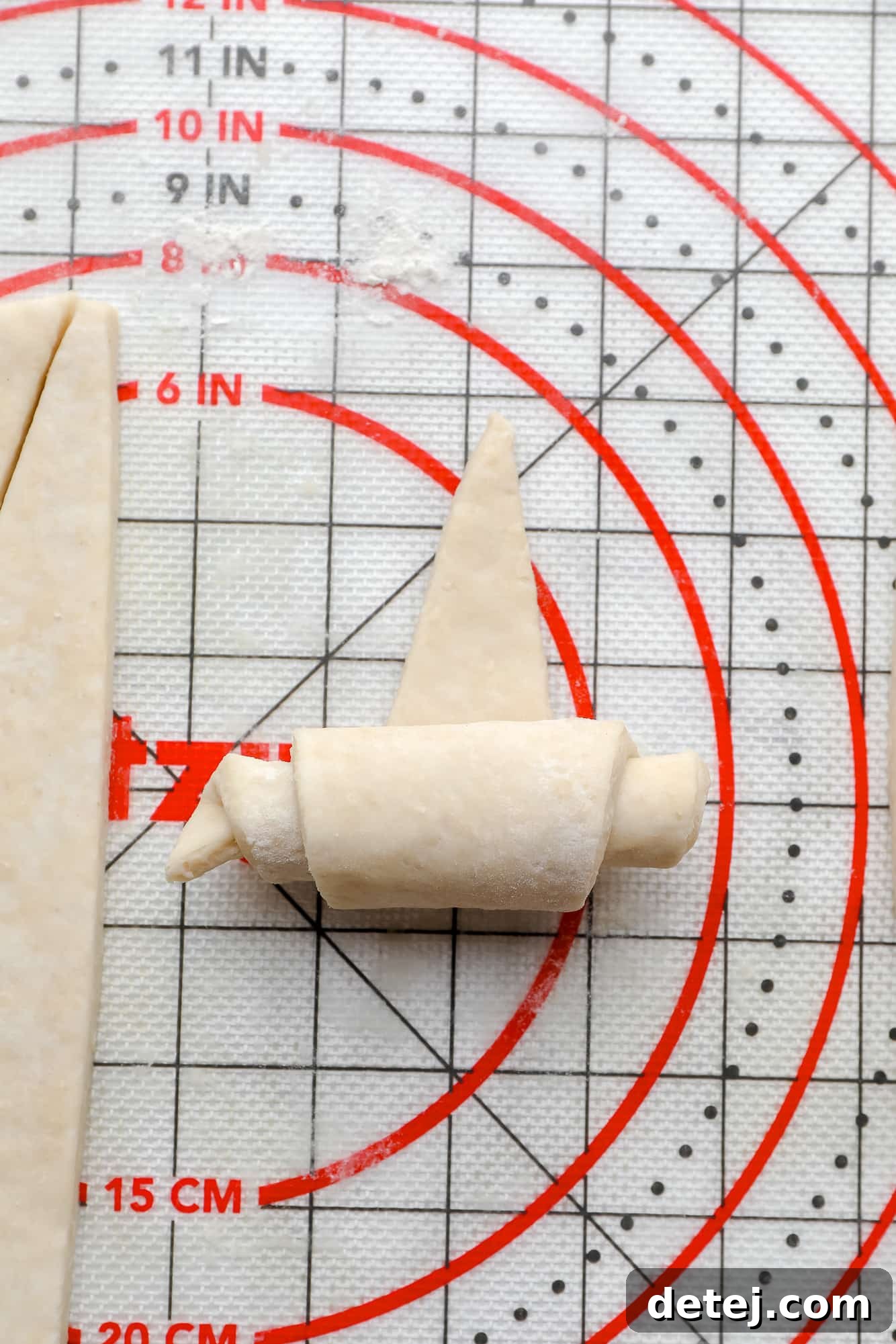 Rolling vegan croissant dough into a perfect crescent shape on a pastry mat.