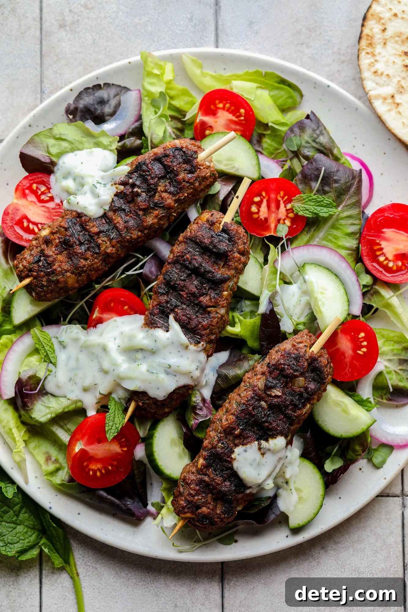 Perfectly grilled vegan kofta skewers resting on a bed of fresh green salad, adorned with colorful vegetables and a generous drizzle of creamy vegan tzatziki.