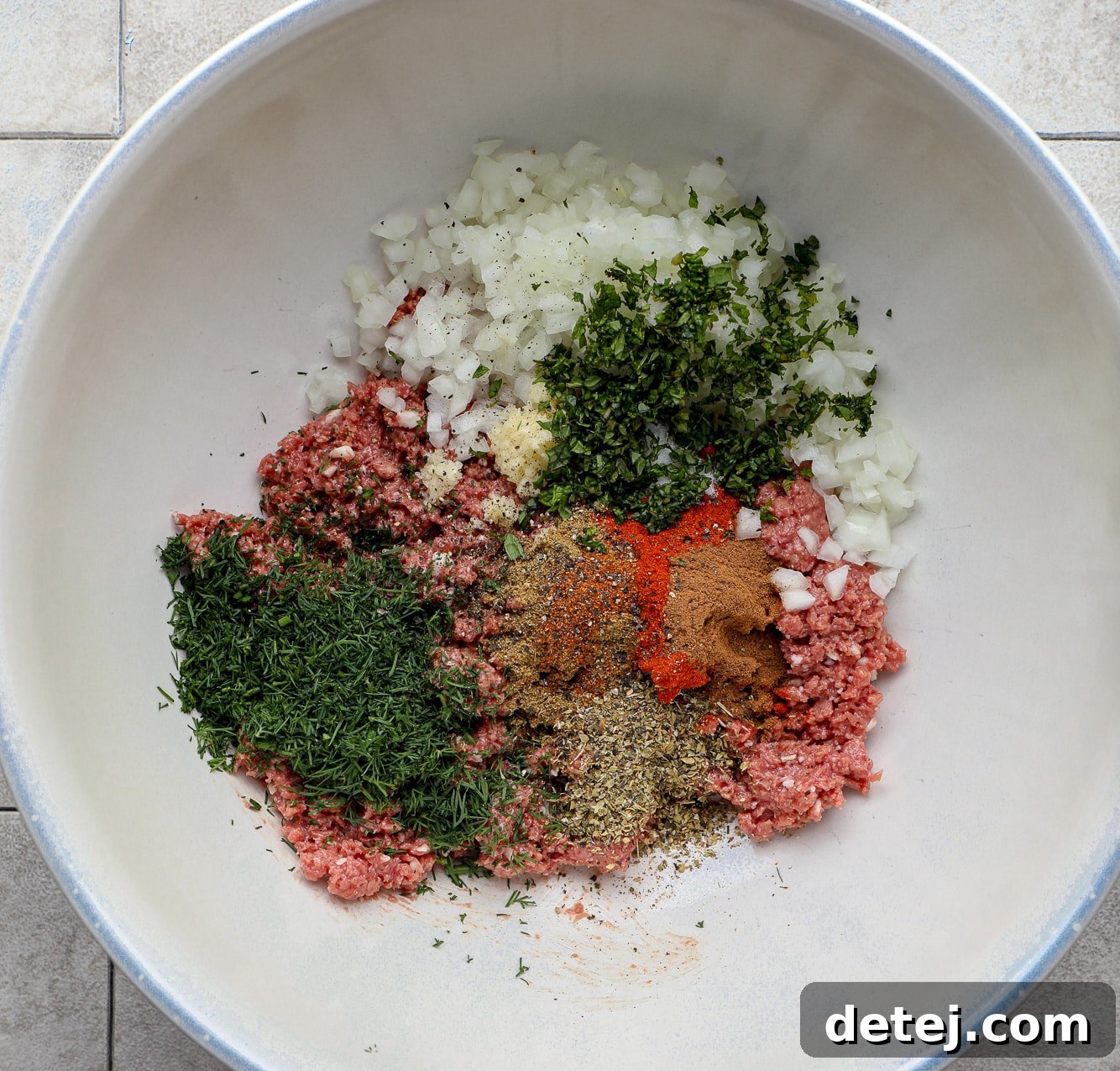 A large white bowl filled with a perfectly combined mixture of vegan ground meat and a medley of aromatic spices and fresh herbs, ready for shaping.