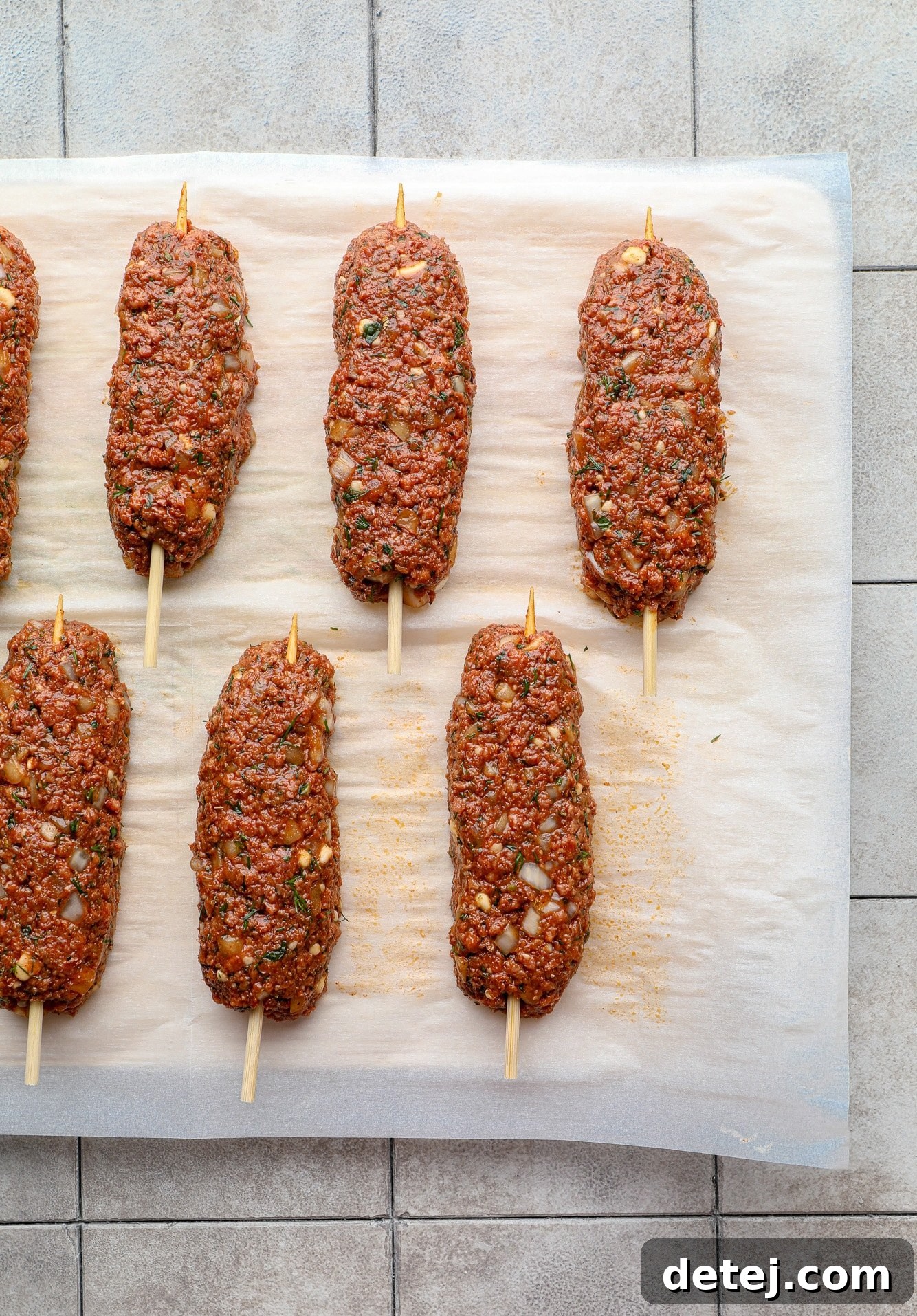 Uncooked vegan kofta logs, skillfully shaped and threaded onto wooden skewers, arranged neatly on a parchment-lined baking sheet, awaiting grilling.