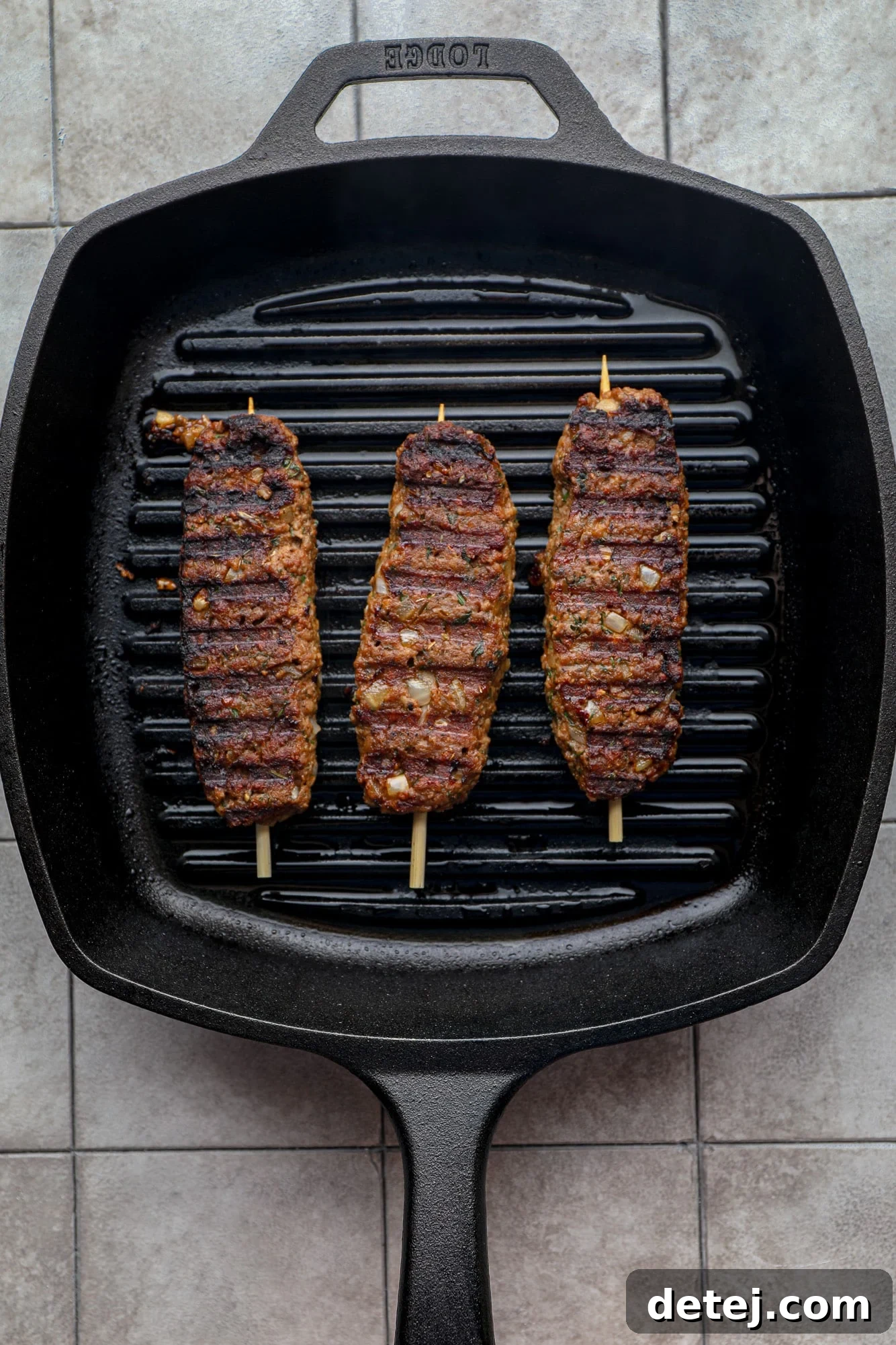Three vegan kofta kebabs sizzling and developing a perfect char on a black grill pan, illustrating the cooking process.