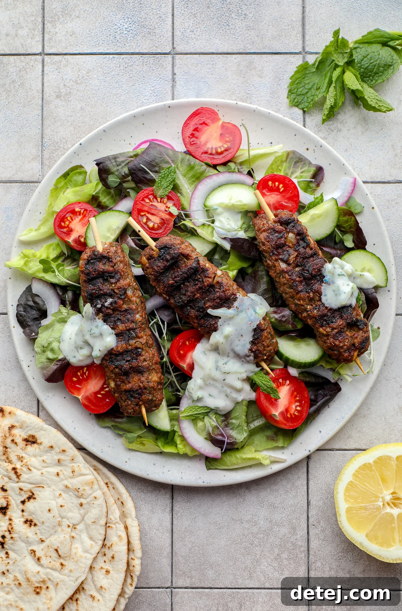 Another enticing shot of grilled vegan kofta presented on a fresh green salad with various vegetables and a generous swirl of tzatziki sauce.