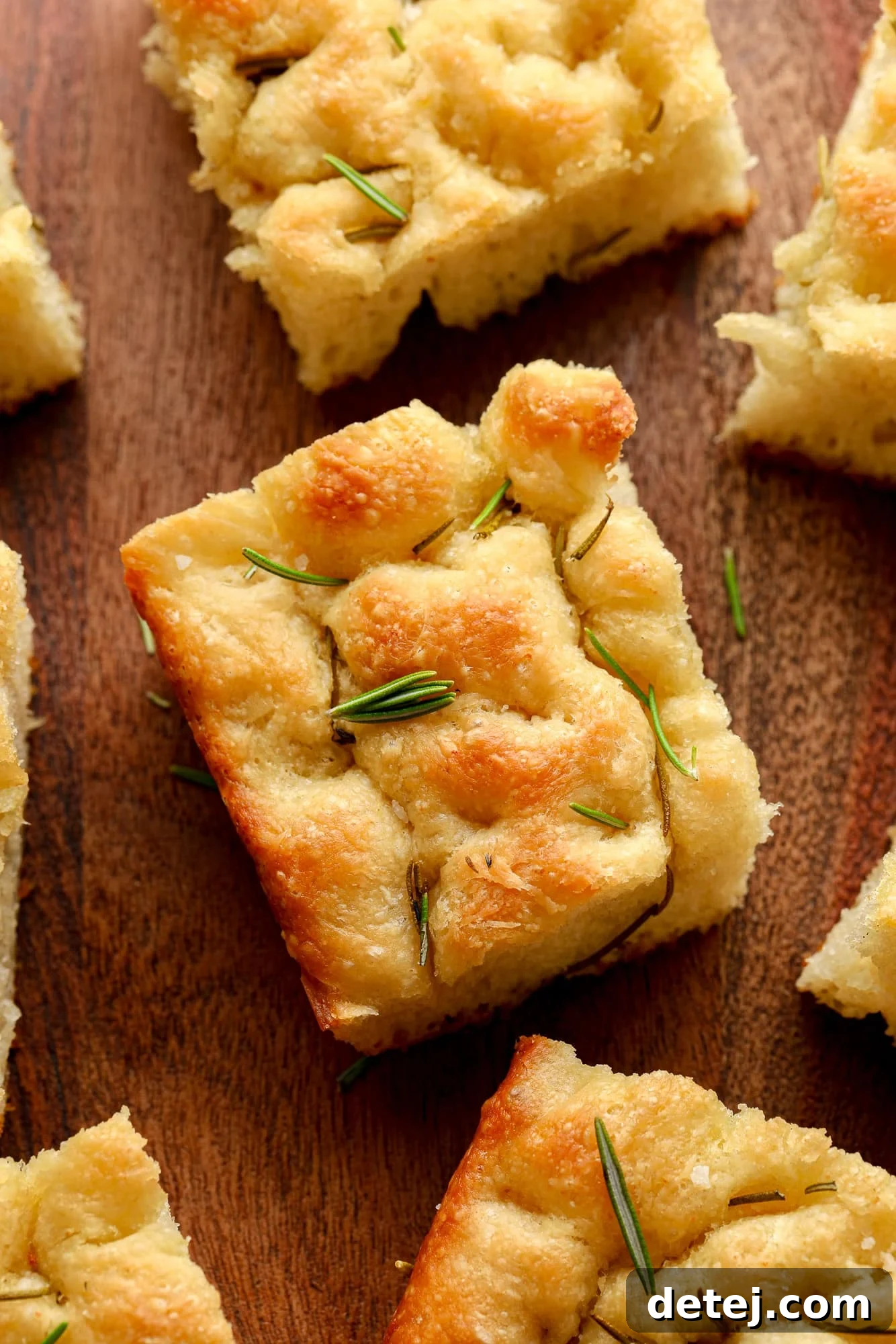 Close up on a slice of homemade vegan focaccia with fresh rosemary and sea salt on top, showcasing its airy texture.