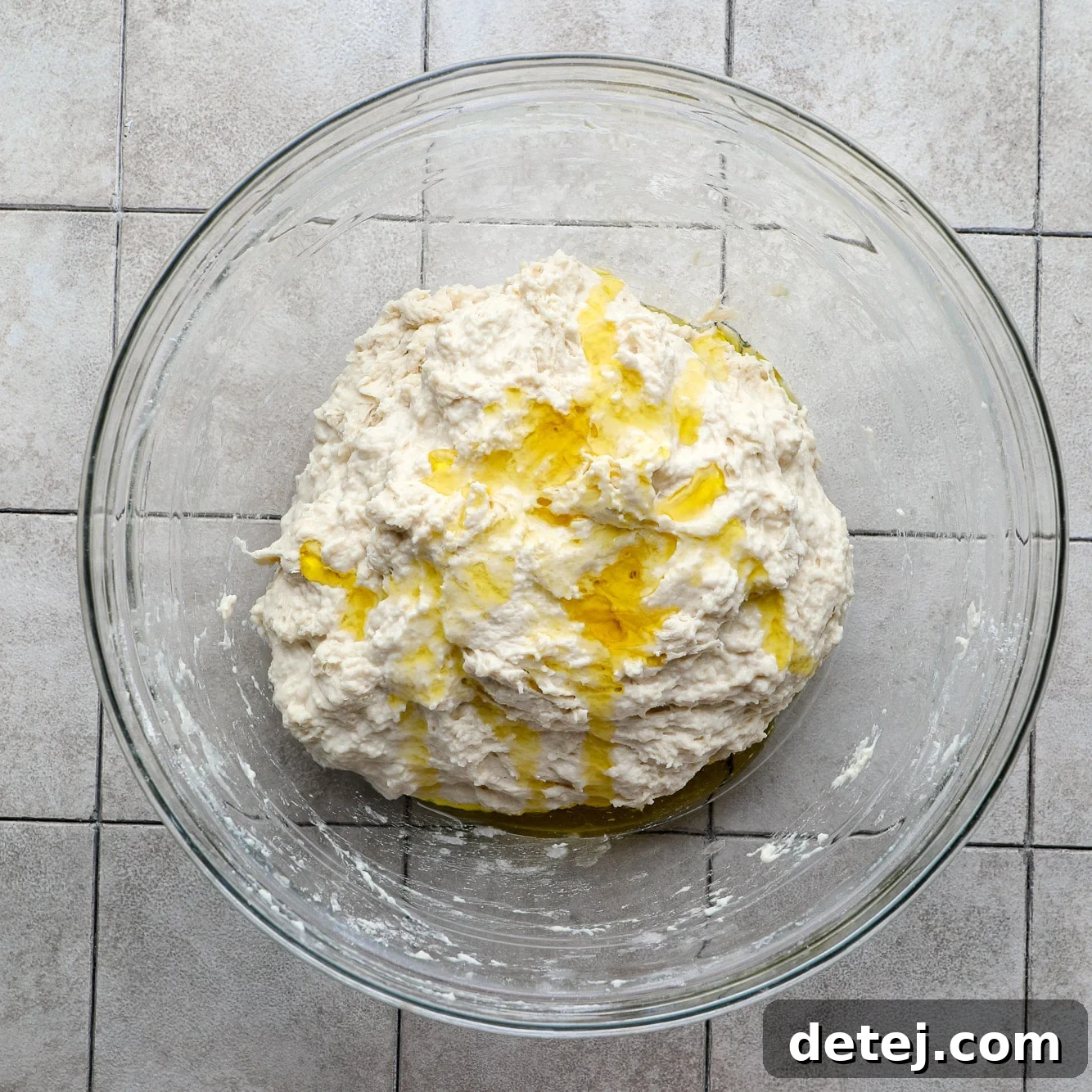 A ball of focaccia dough glistening with olive oil in a glass bowl.