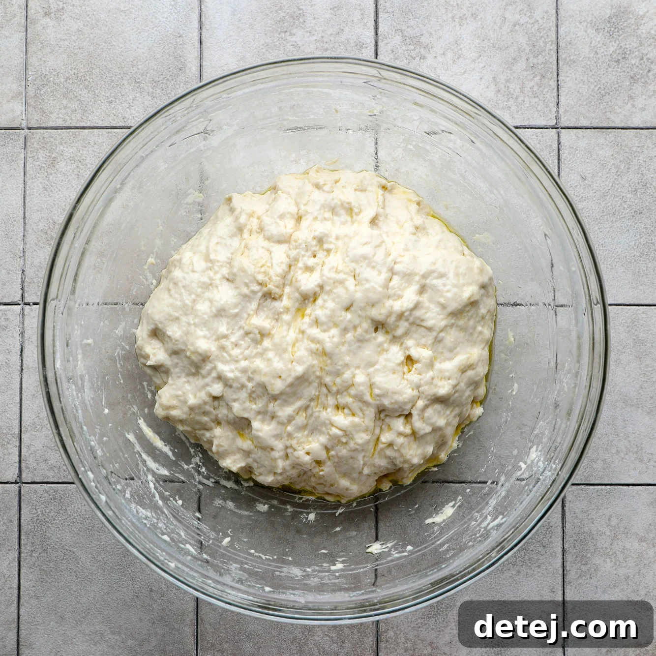 A ball of vegan focaccia dough covered with a damp tea towel in a glass bowl, ready for its long cold rise.