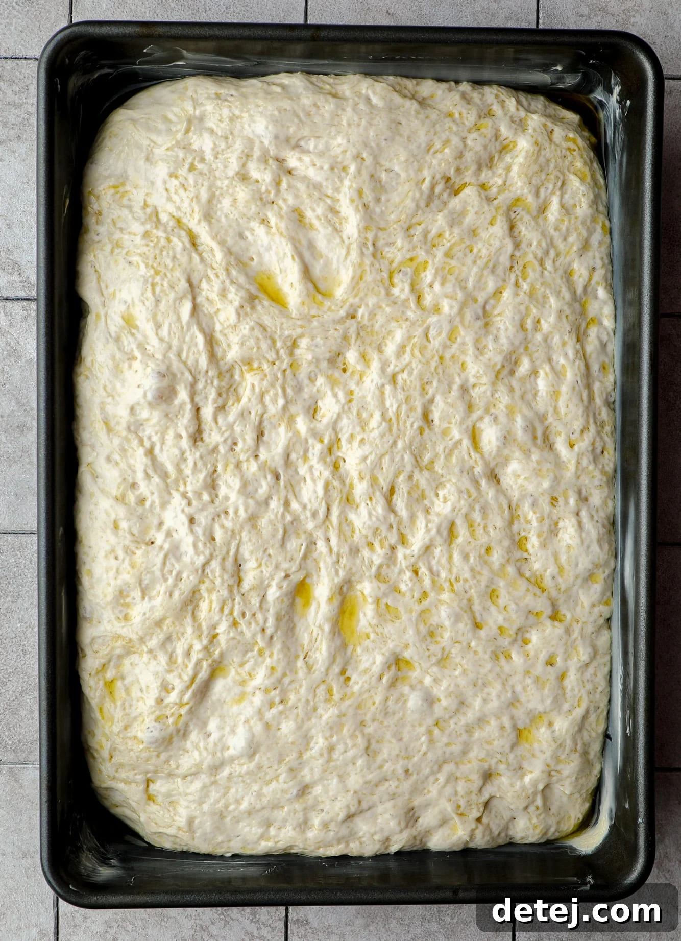 Focaccia dough, having expanded, filling a large black baking pan.