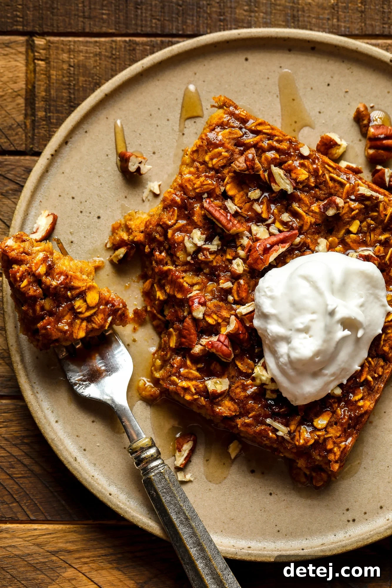 A beautifully presented slice of vegan pumpkin baked oatmeal, topped with a dollop of creamy vegan whipped cream, served on a rustic brown plate. The warm hues evoke cozy fall mornings.