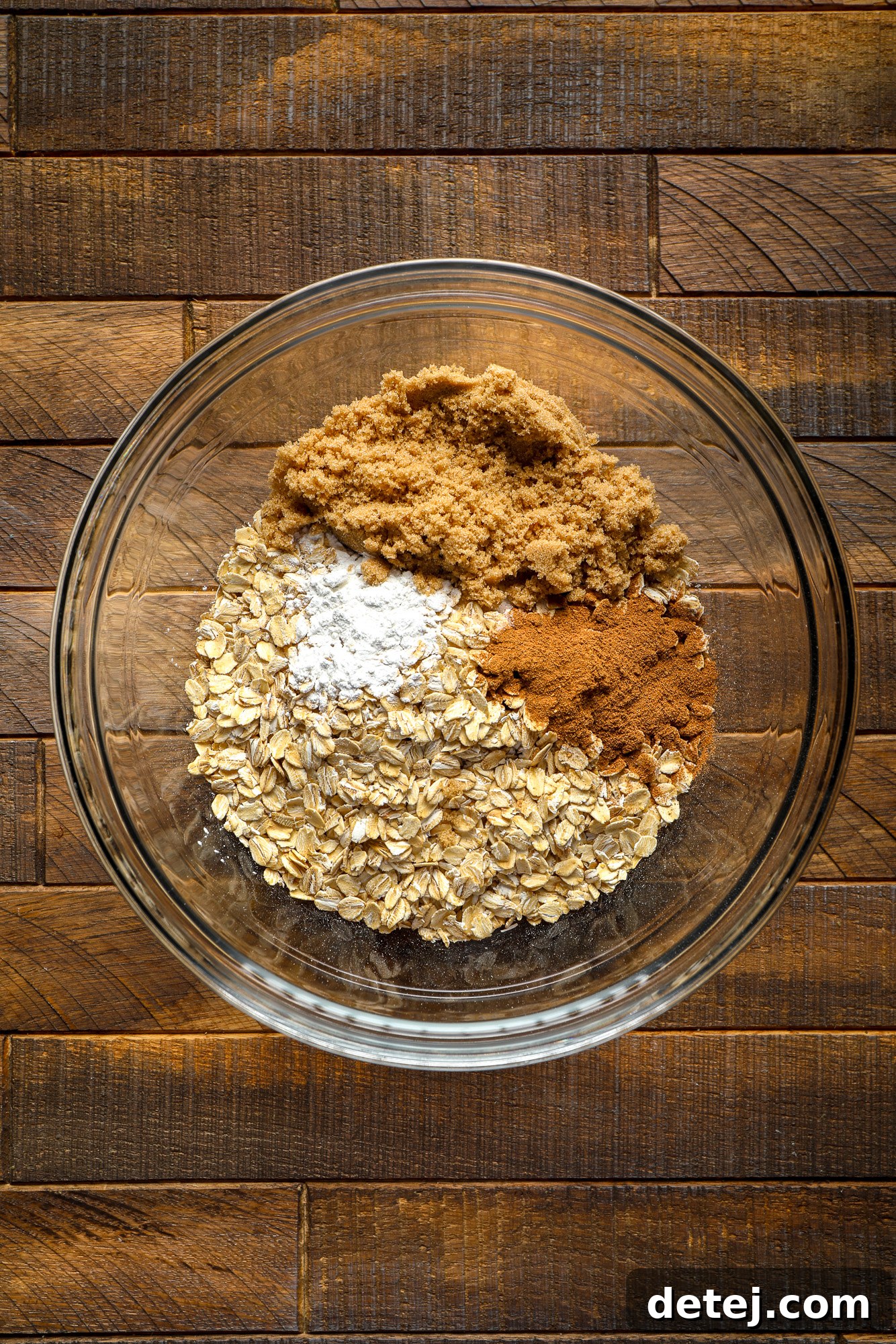 A clear glass bowl showcasing the perfectly mixed dry ingredients for pumpkin baked oatmeal: rolled oats, baking powder, pumpkin pie spice, and salt.