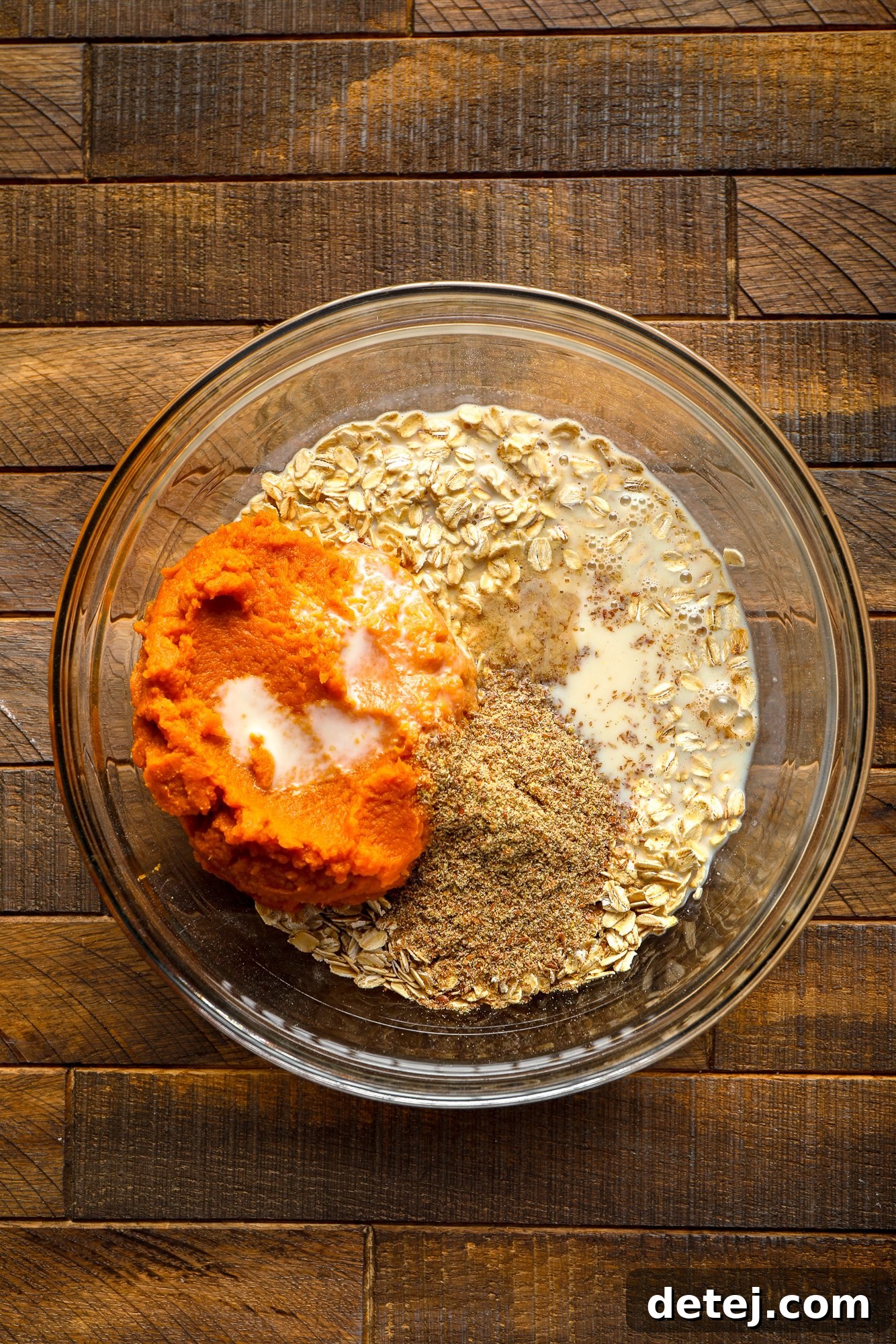 All ingredients for vegan pumpkin baked oatmeal, including wet and dry components, thoroughly mixed together in a large glass bowl, ready for baking.