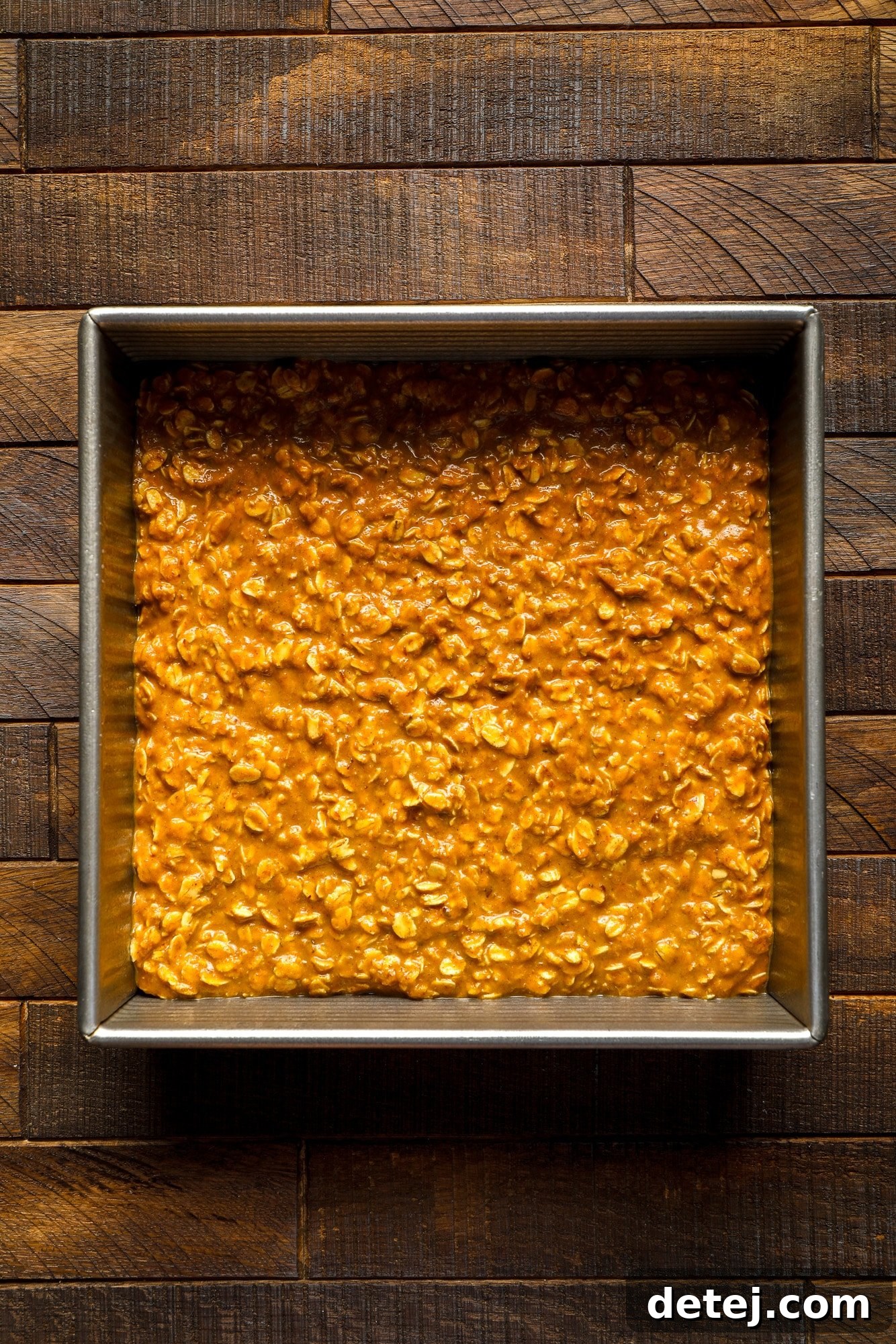 Unbaked vegan pumpkin oatmeal mixture spread evenly in a square metal baking pan, ready to be placed in the oven.