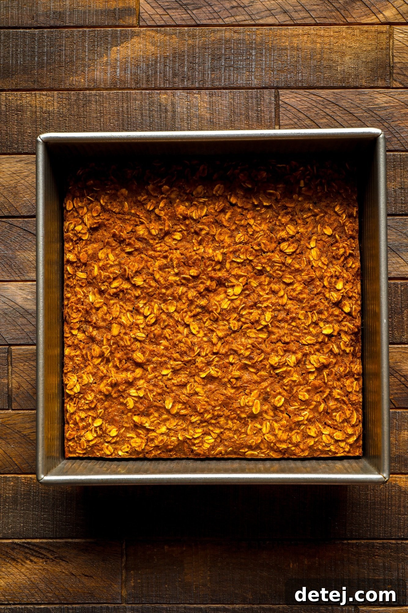 Freshly baked vegan pumpkin oatmeal, golden and puffed around the edges, still warm in a square metal baking pan.
