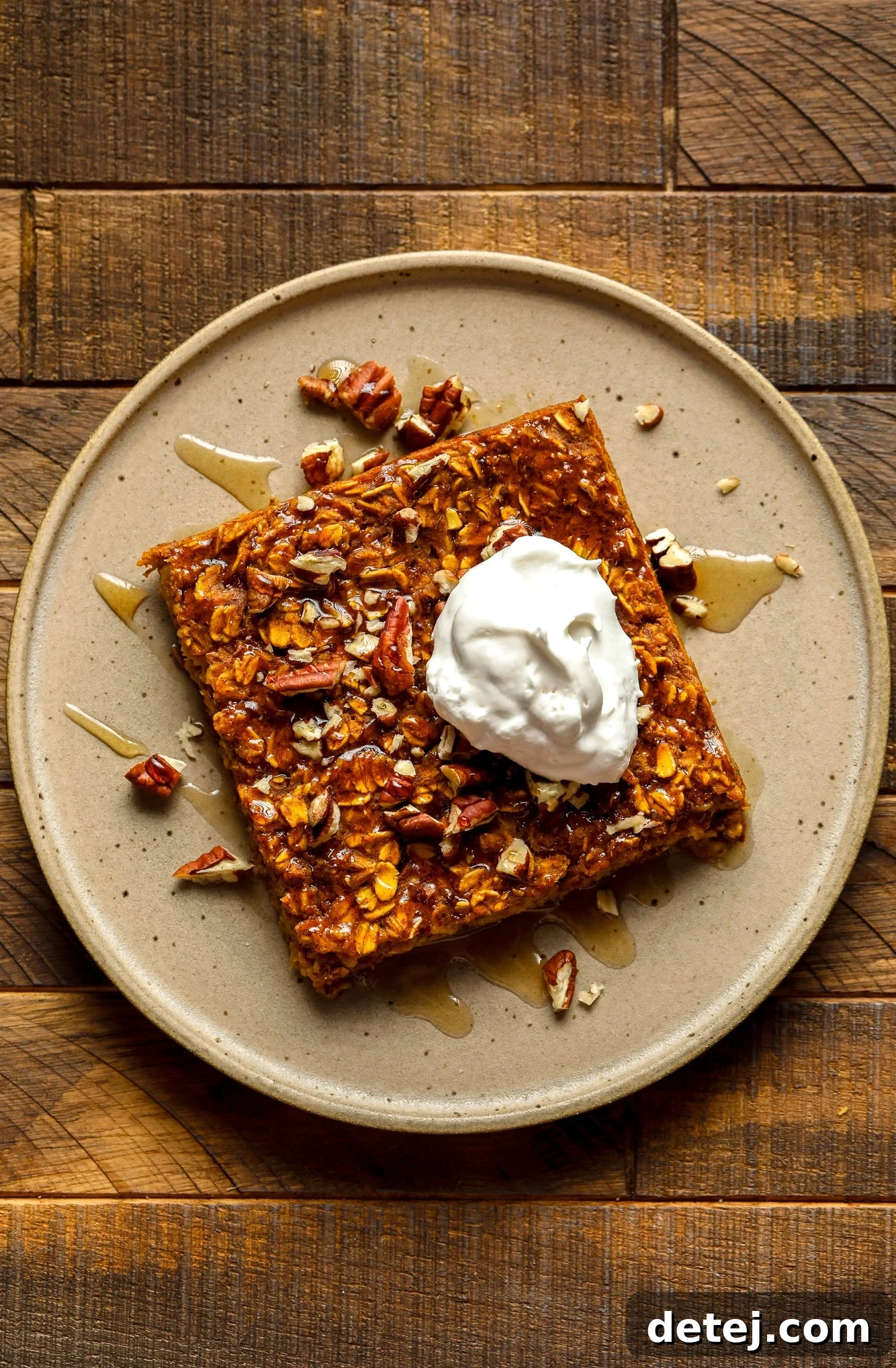 A single slice of vegan pumpkin baked oatmeal, elegantly presented on a brown plate and adorned with a dollop of fluffy vegan whipped cream, highlighting its inviting texture.