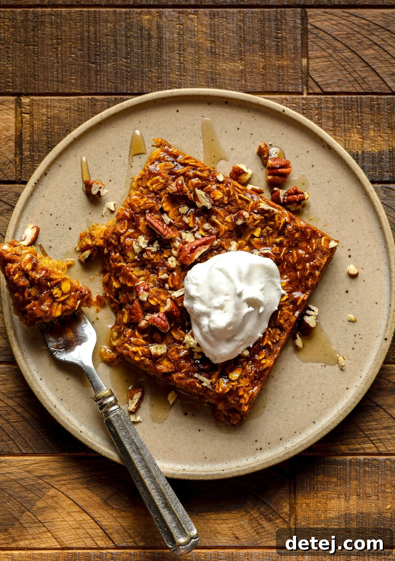 A close-up shot of a single slice of vegan pumpkin baked oatmeal, elegantly positioned on a brown plate with a dollop of vegan whipped cream, ready to be enjoyed.