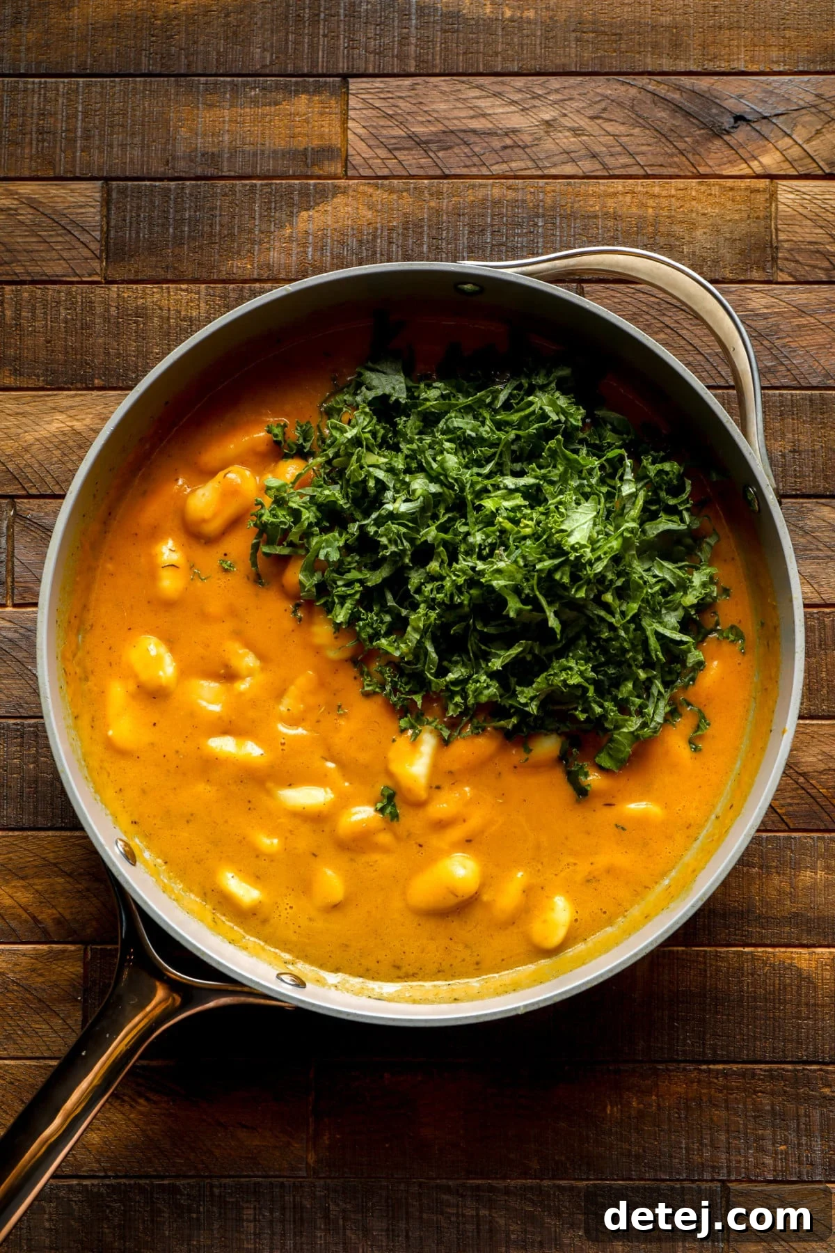 a pot of pumpkin gnocchi with chopped kale on top.