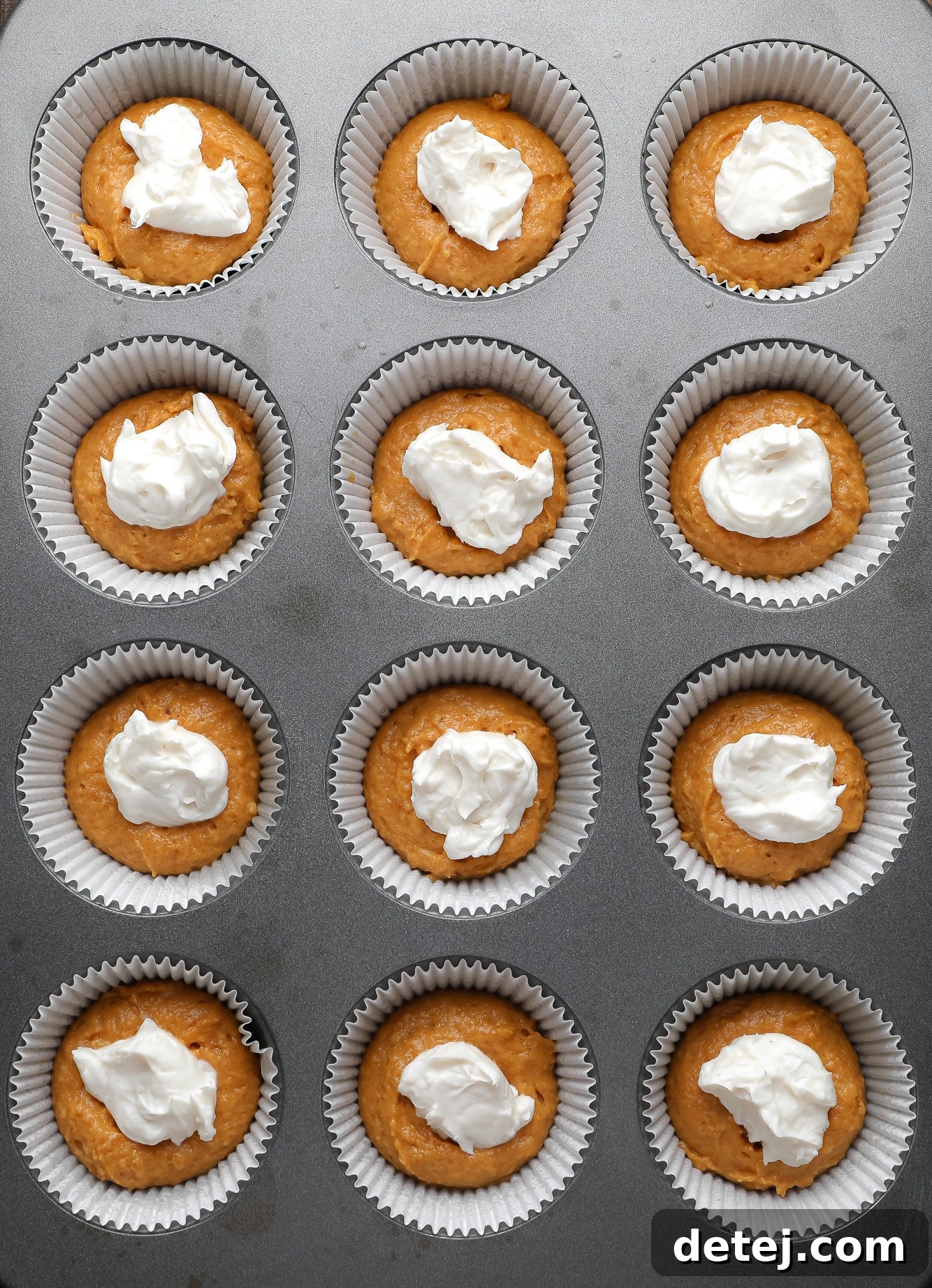 Vegan Pumpkin Cheesecake Swirl Muffins 3 a muffin tin filled with vegan pumpkin muffin batter topped with dollops of vegan cream cheese.