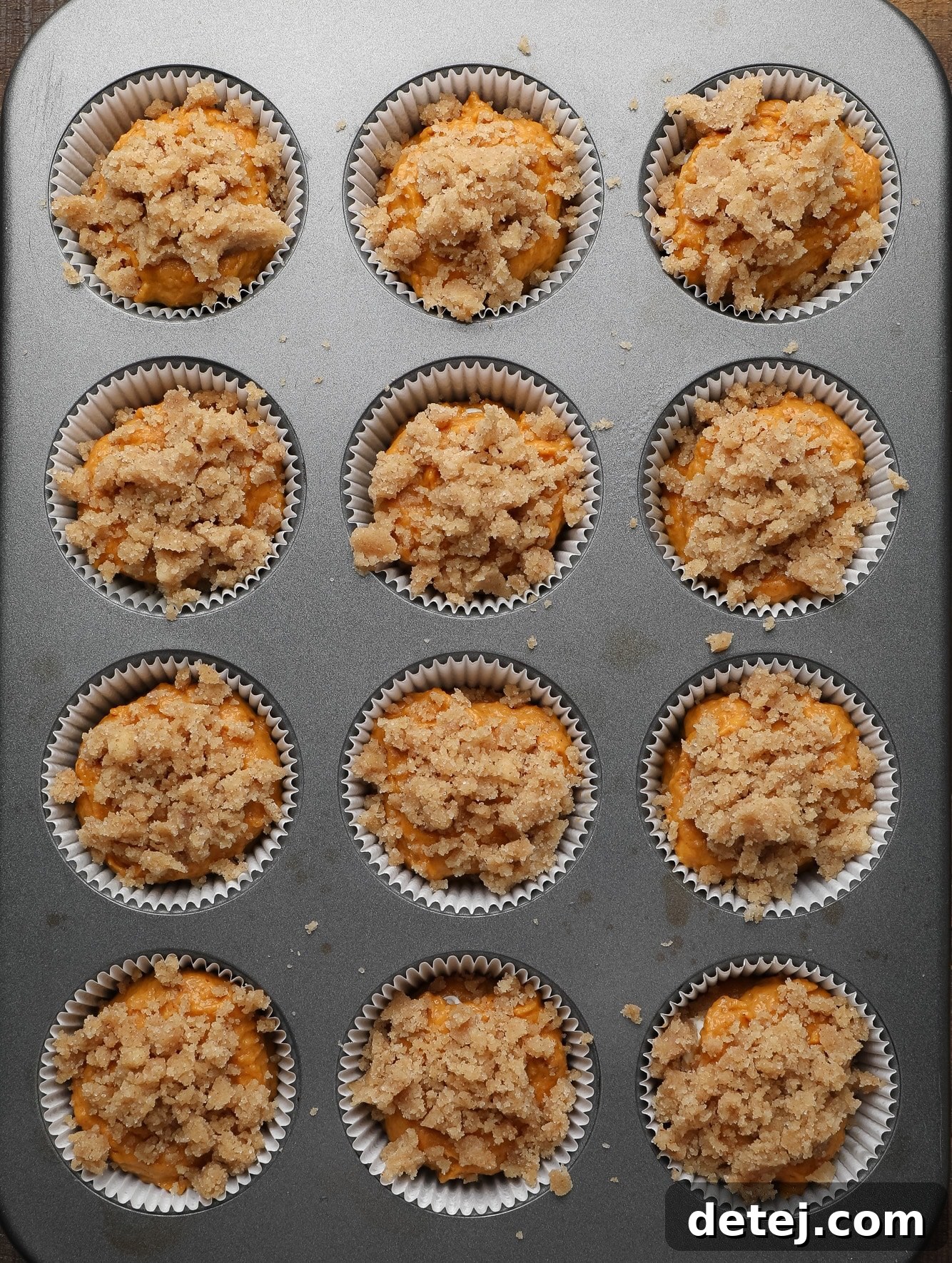 Vegan Pumpkin Cheesecake Swirl Muffins 4 unbaked vegan pumpkin cream cheese muffins topped with cinnamon streusel in a muffin tin.