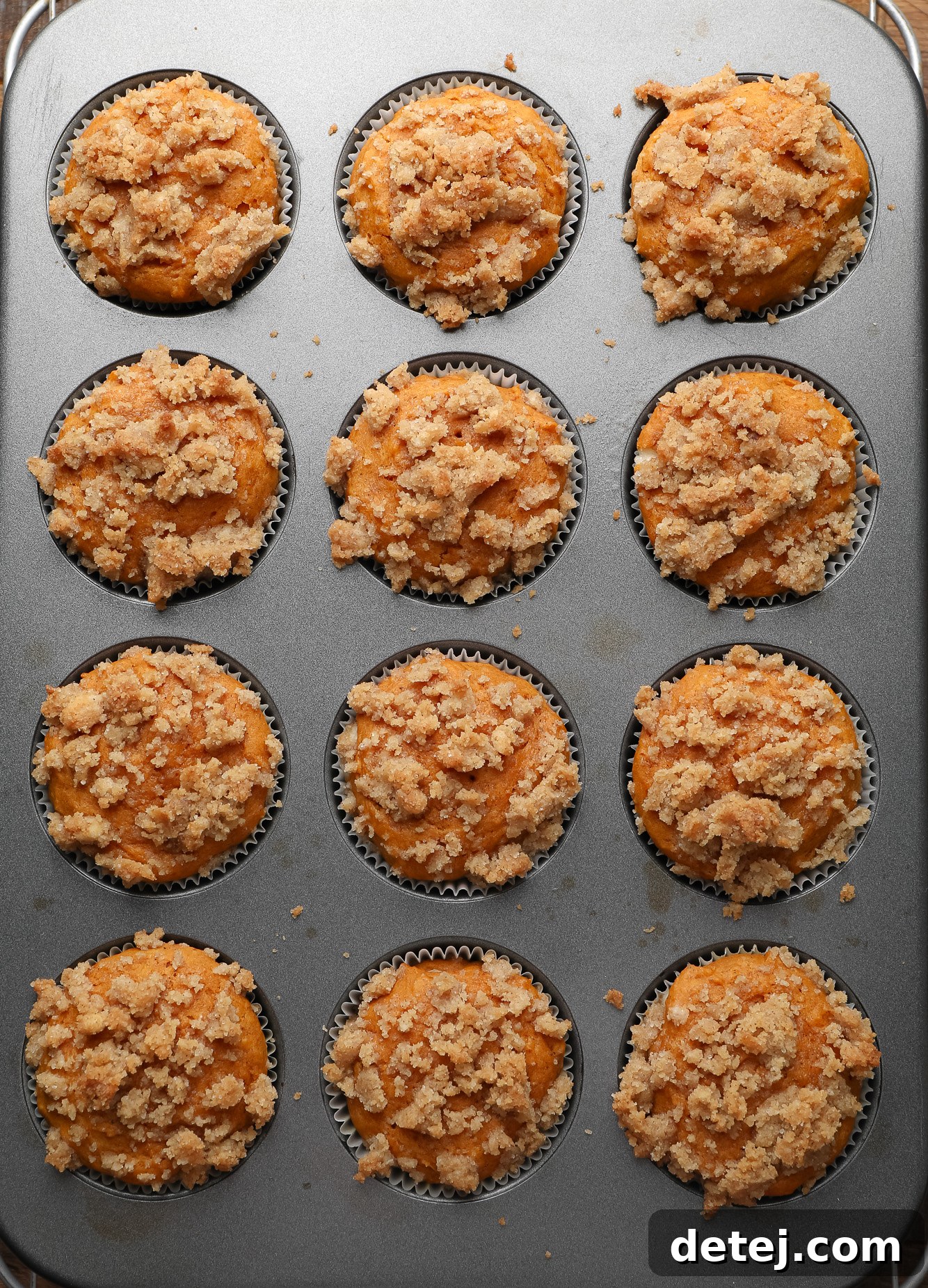 Vegan Pumpkin Cheesecake Swirl Muffins 5 baked vegan pumpkin cream cheese muffins topped with cinnamon streusel in a muffin tin.