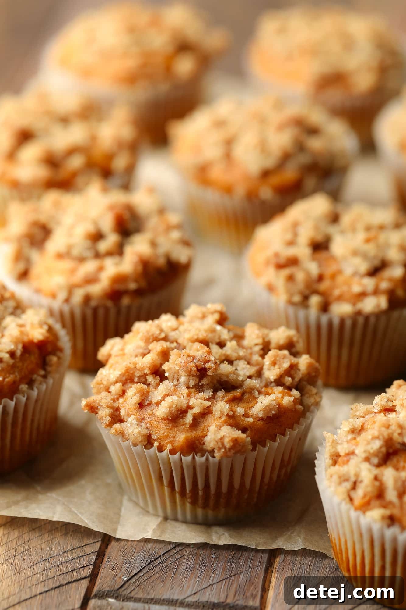 Vegan Pumpkin Cheesecake Swirl Muffins 6 rows of baked vegan pumpkin cream cheese muffins on a piece of parchment paper.