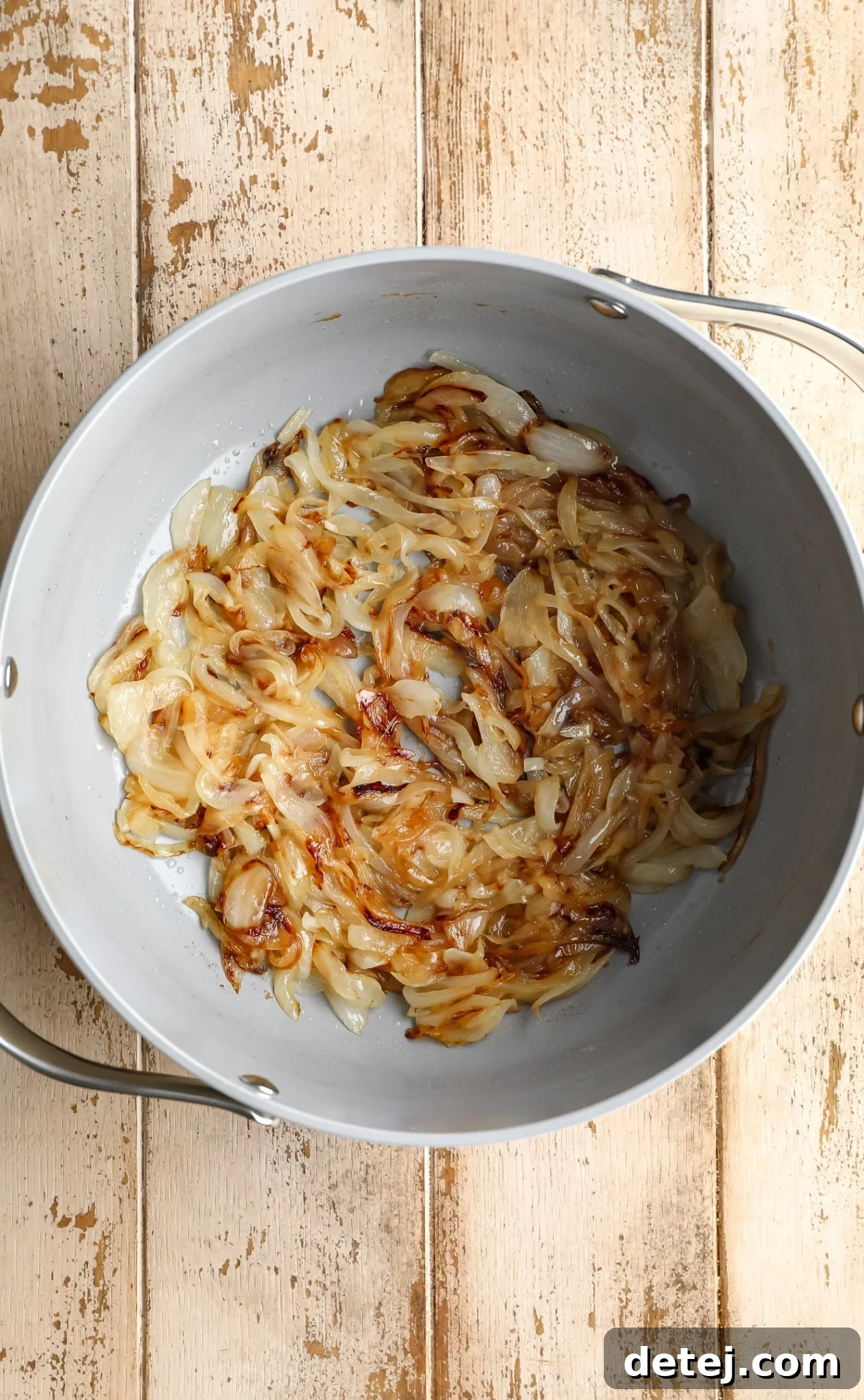 Sliced yellow onions slowly caramelizing to a golden brown in a grey pot, creating a sweet and savory base for the soup.