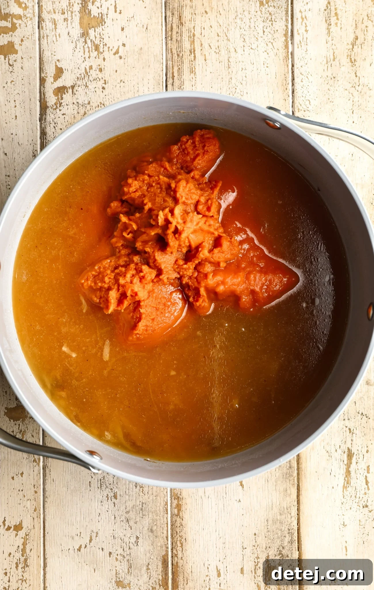 All the core ingredients for vegan pumpkin soup, including pumpkin puree and vegetable broth, combined in a large grey pot, ready for simmering.