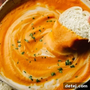 close up of a piece of bread being dipped in a bowl of vegan pumpkin soup.