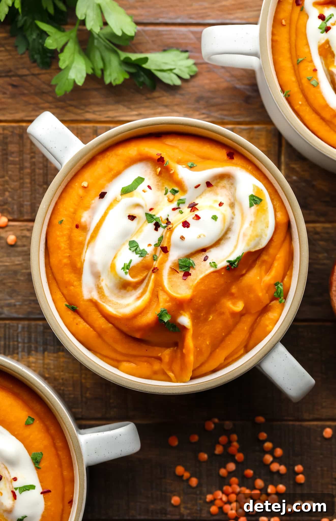carrot lentil soup topped with vegan yogurt and green herbs in a white soup bowl.