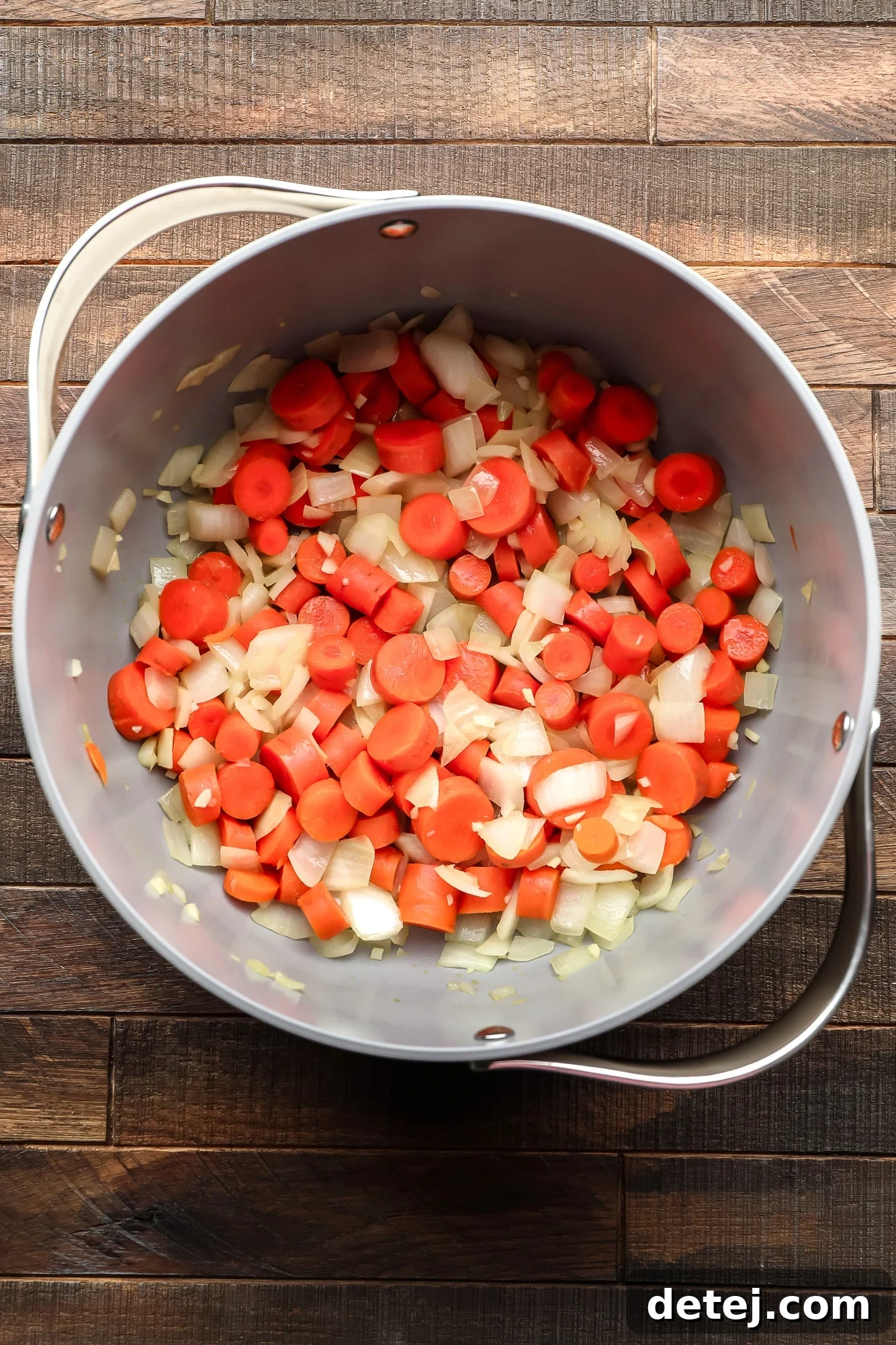 cooking chopped carrots, onions, and garlic in a large grey pot.