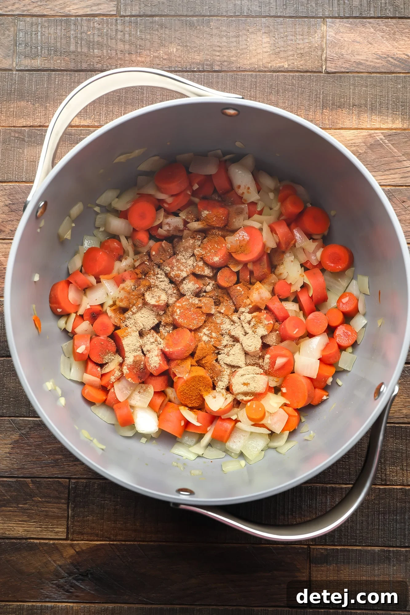 chopped carrots, onions, and garlic coated in spices in a large grey pot.