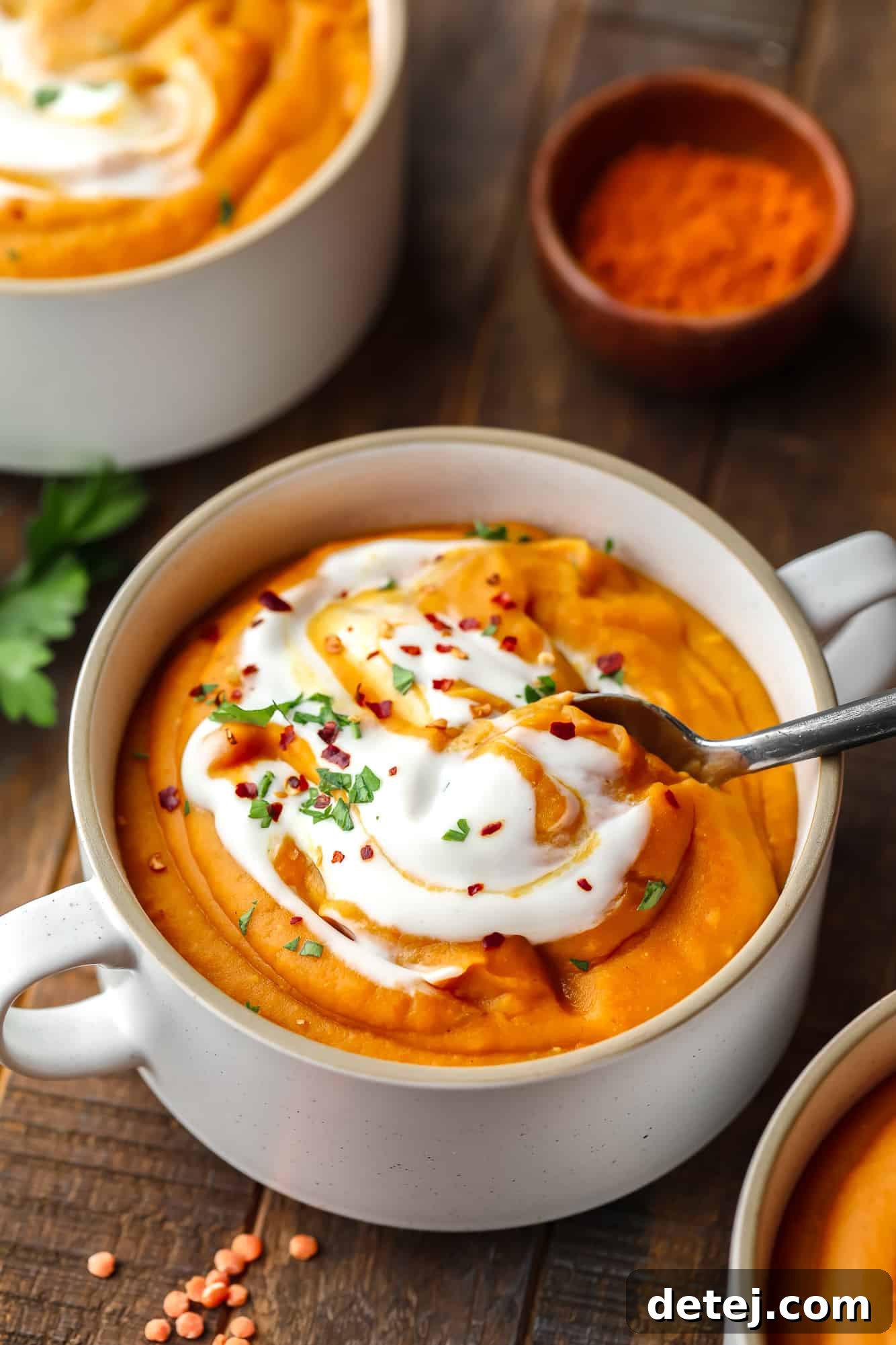 using a metal spoon to lift a scoop of carrot lentil soup from a white soup bowl.