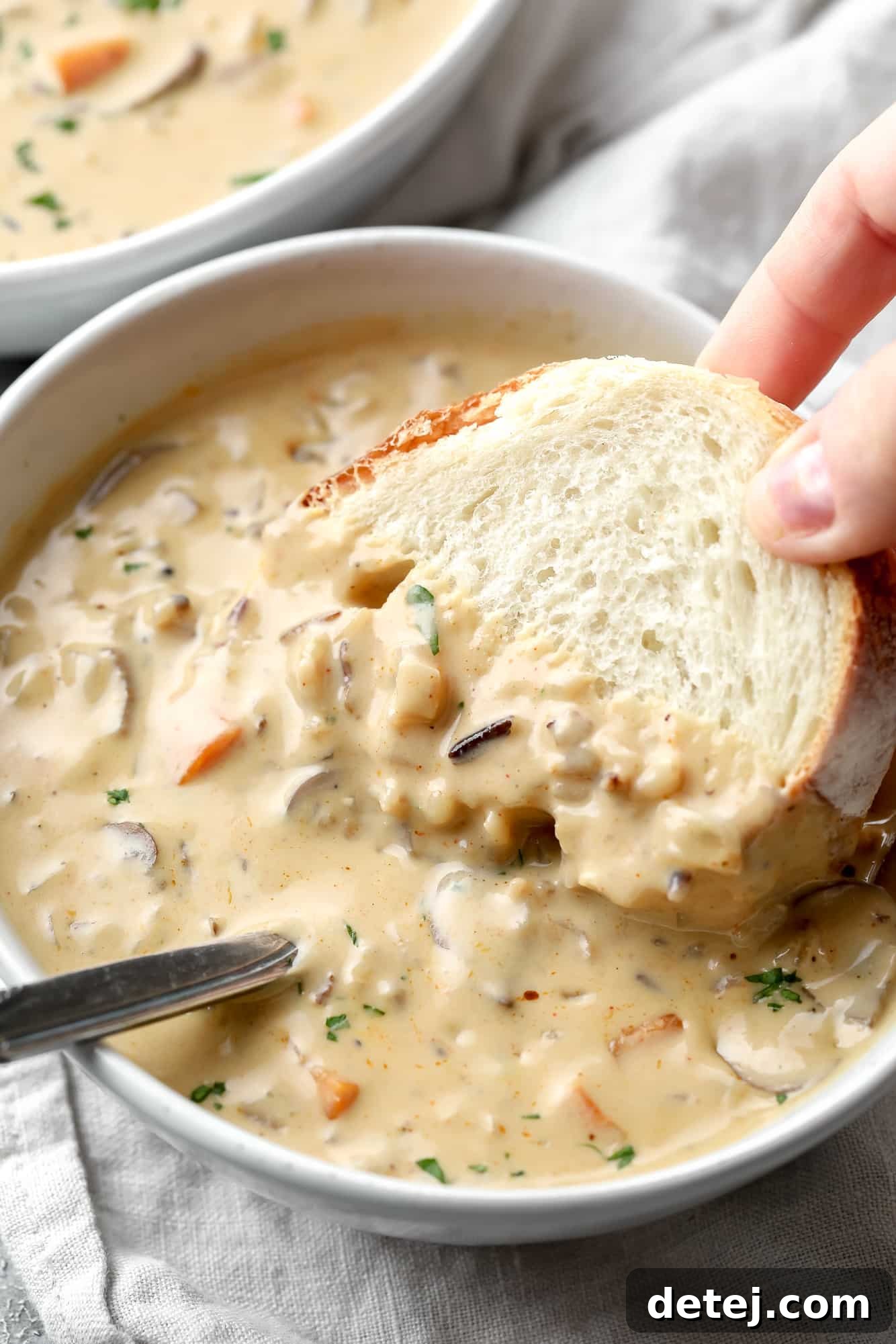 womans hand dipping a piece of bread into a bowl of vegan mushroom soup.