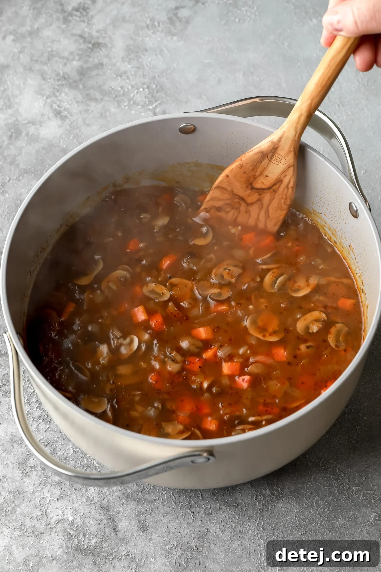using a wooden spoon to stir mushroom soup in a large grey pot.