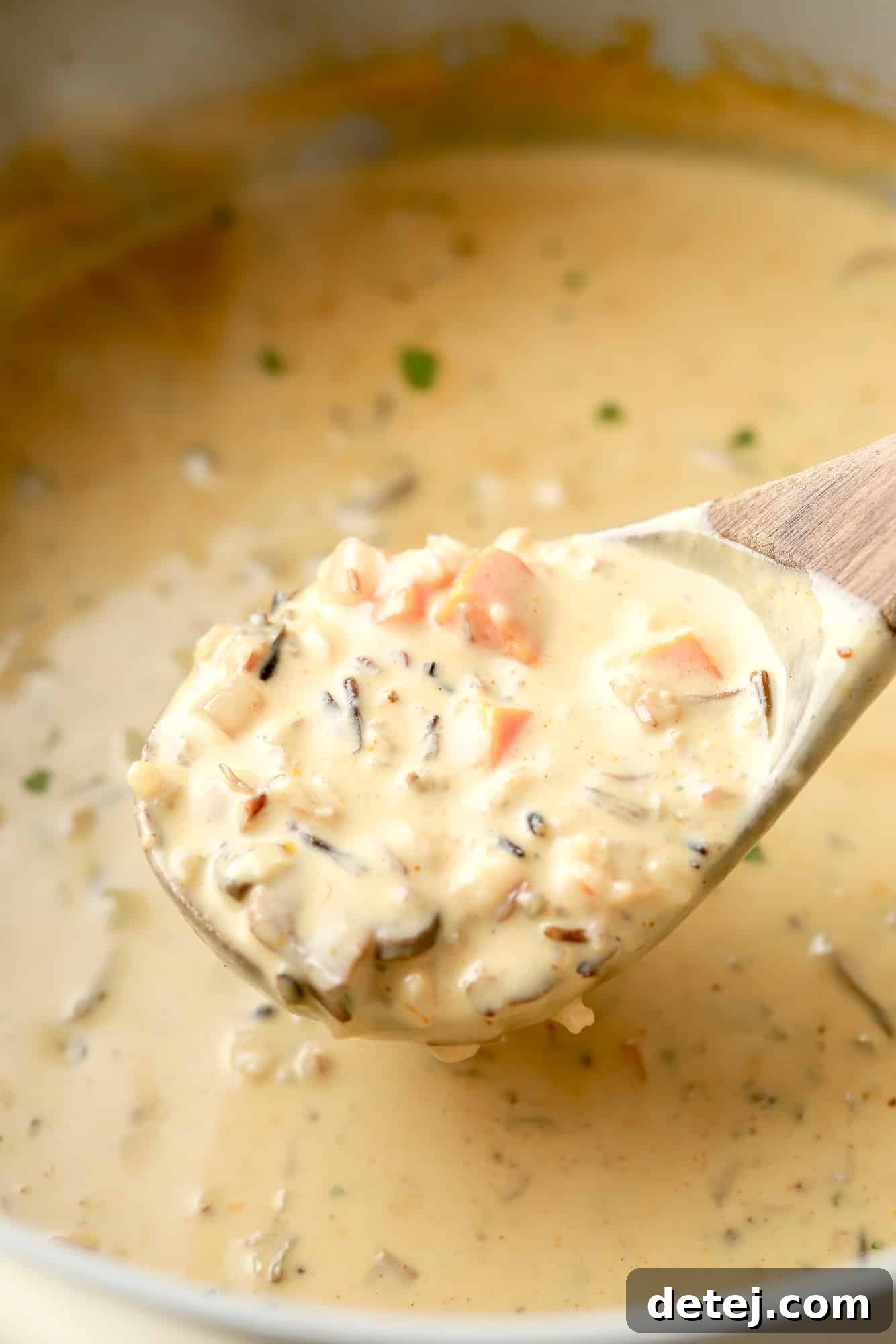 using a wooden spoon to lift a scoop of vegan mushroom soup from a large batch.