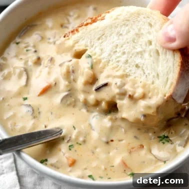 womans hand dipping a piece of bread into a bowl of vegan mushroom soup.