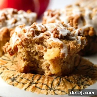 A beautifully glazed vegan apple muffin with a bite taken out, resting on a white board, showcasing its fluffy interior and crumb topping.