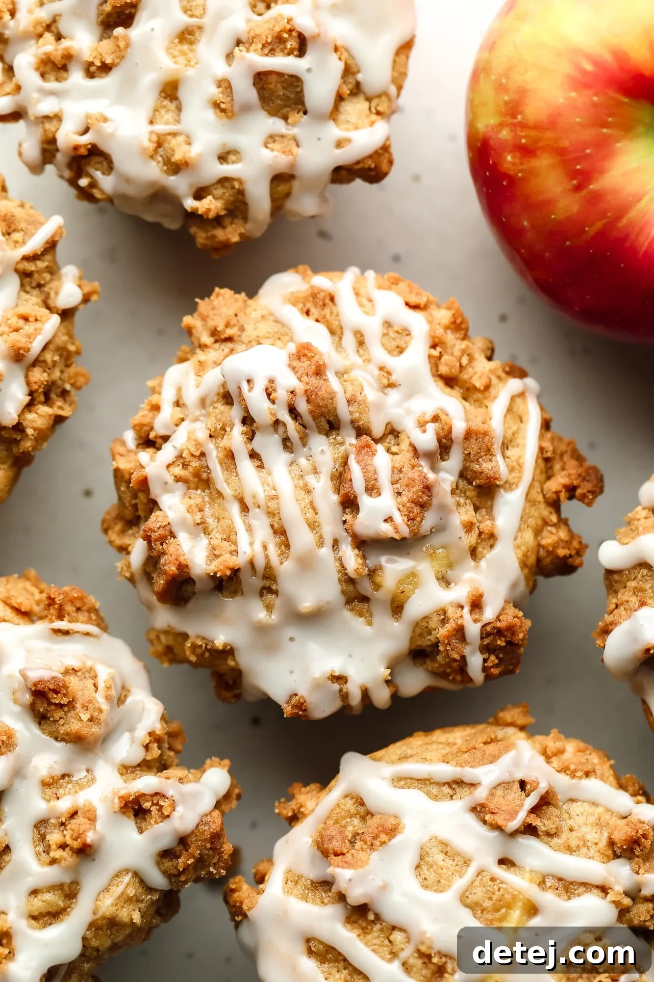 Overhead view of several baked vegan apple muffins, beautifully topped with a golden crumb and delicate white vanilla icing.