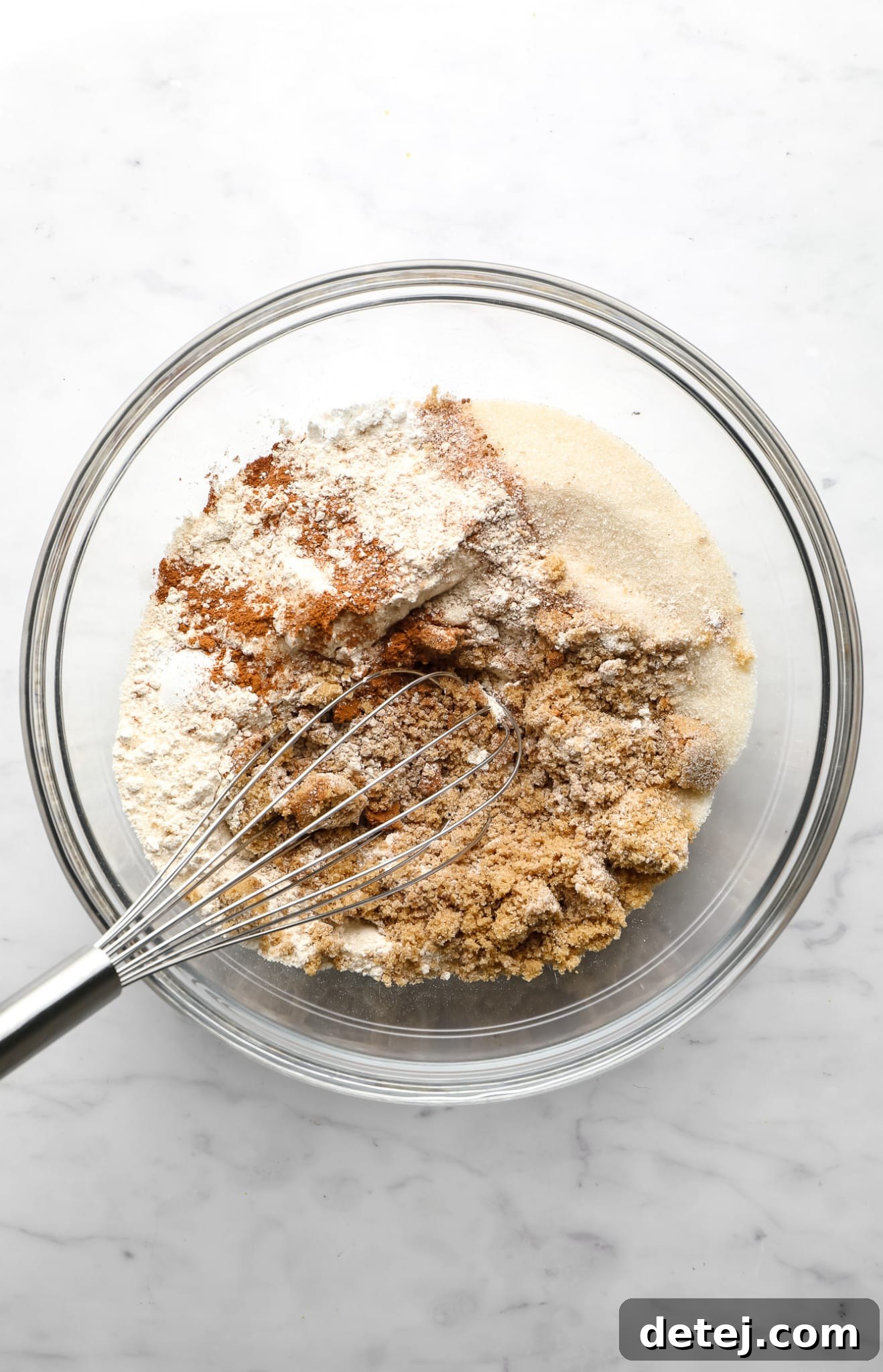 Image showing dry ingredients for vegan apple muffins being whisked together in a clear glass bowl.