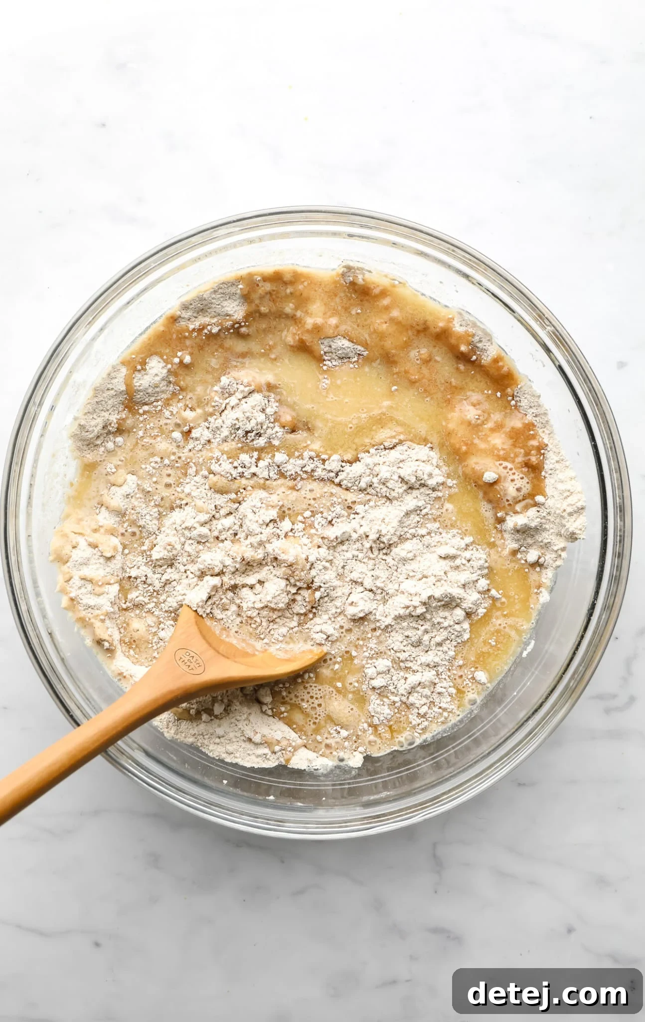 Image showing vegan apple muffin batter being gently stirred with a wooden spoon in a glass bowl.